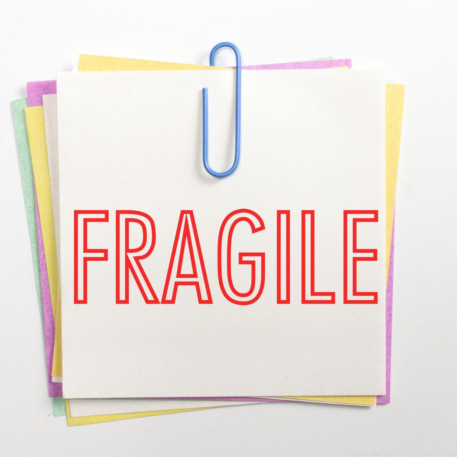 Slim Pre-Inked Fragile Stamp marking FRAGILE in red on a stack of colorful sticky notes held by a blue paperclip.