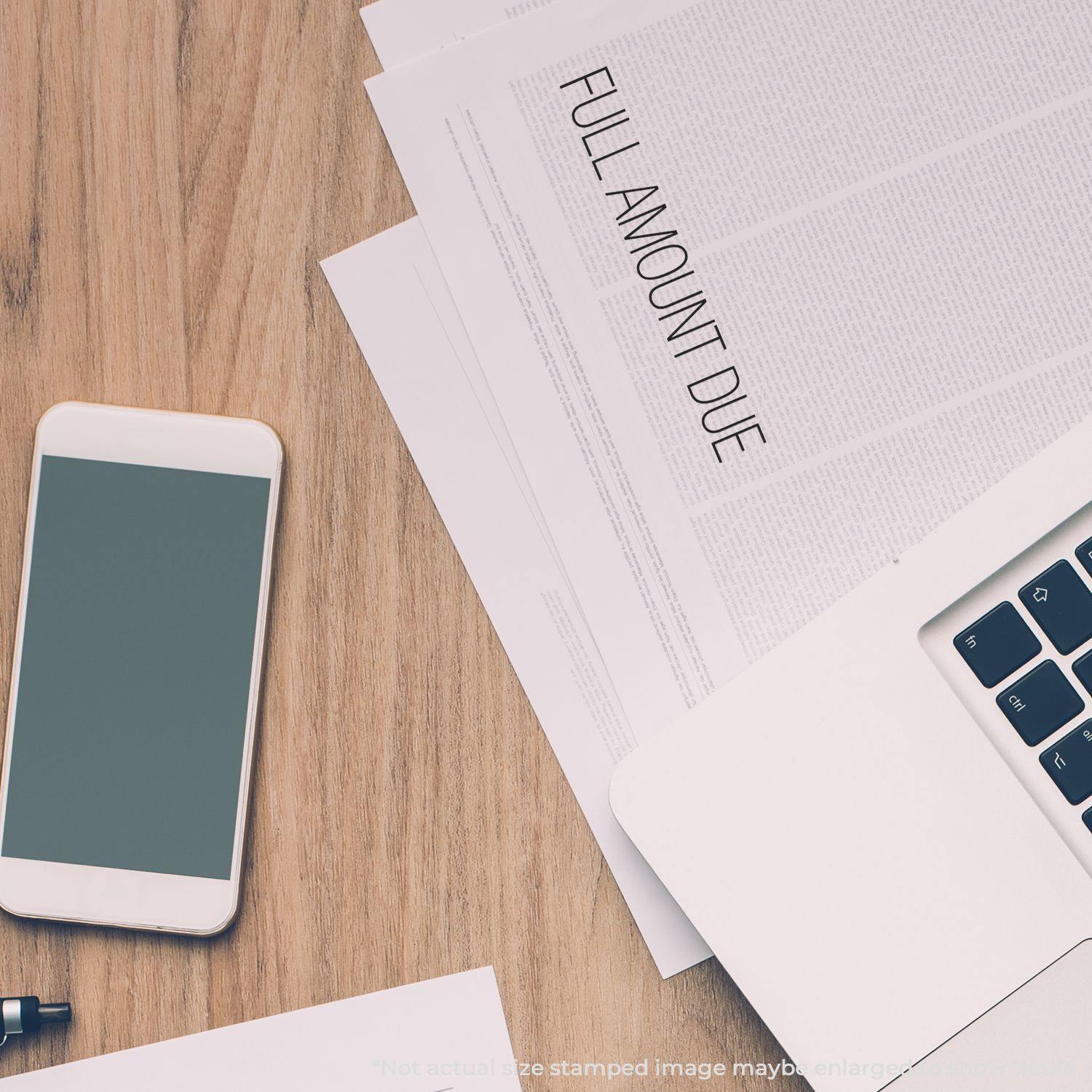 Full Amount Due Rubber Stamp used on a document placed on a wooden desk with a smartphone, pen, and laptop nearby.