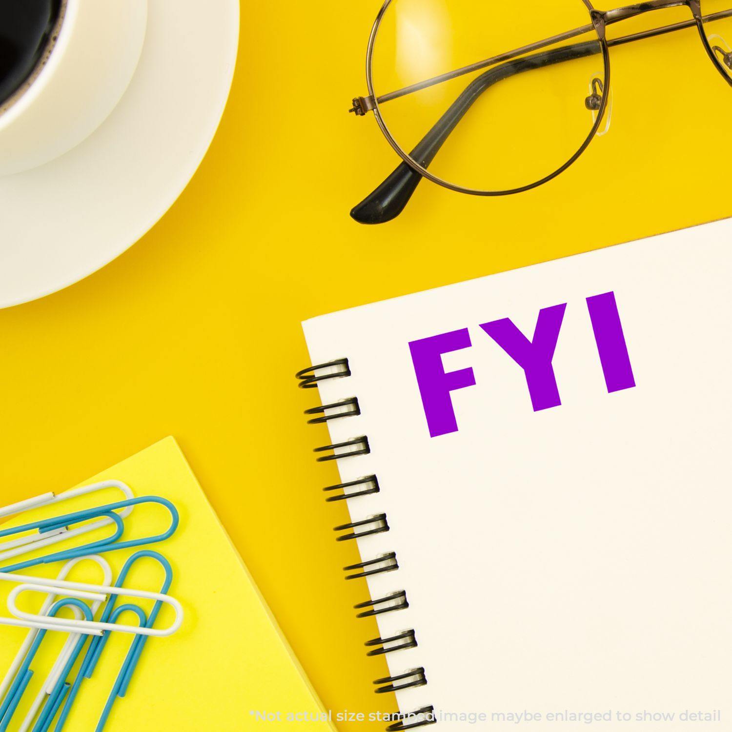 A Large FYI Rubber Stamp imprint in purple ink on a white notebook, surrounded by a coffee cup, glasses, and colorful paperclips on a yellow background.