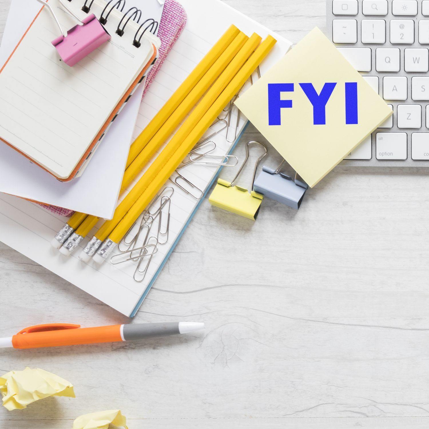 Desk with notepad, pencils, paper clips, sticky notes stamped with FYI using Large FYI Rubber Stamp, and a keyboard.