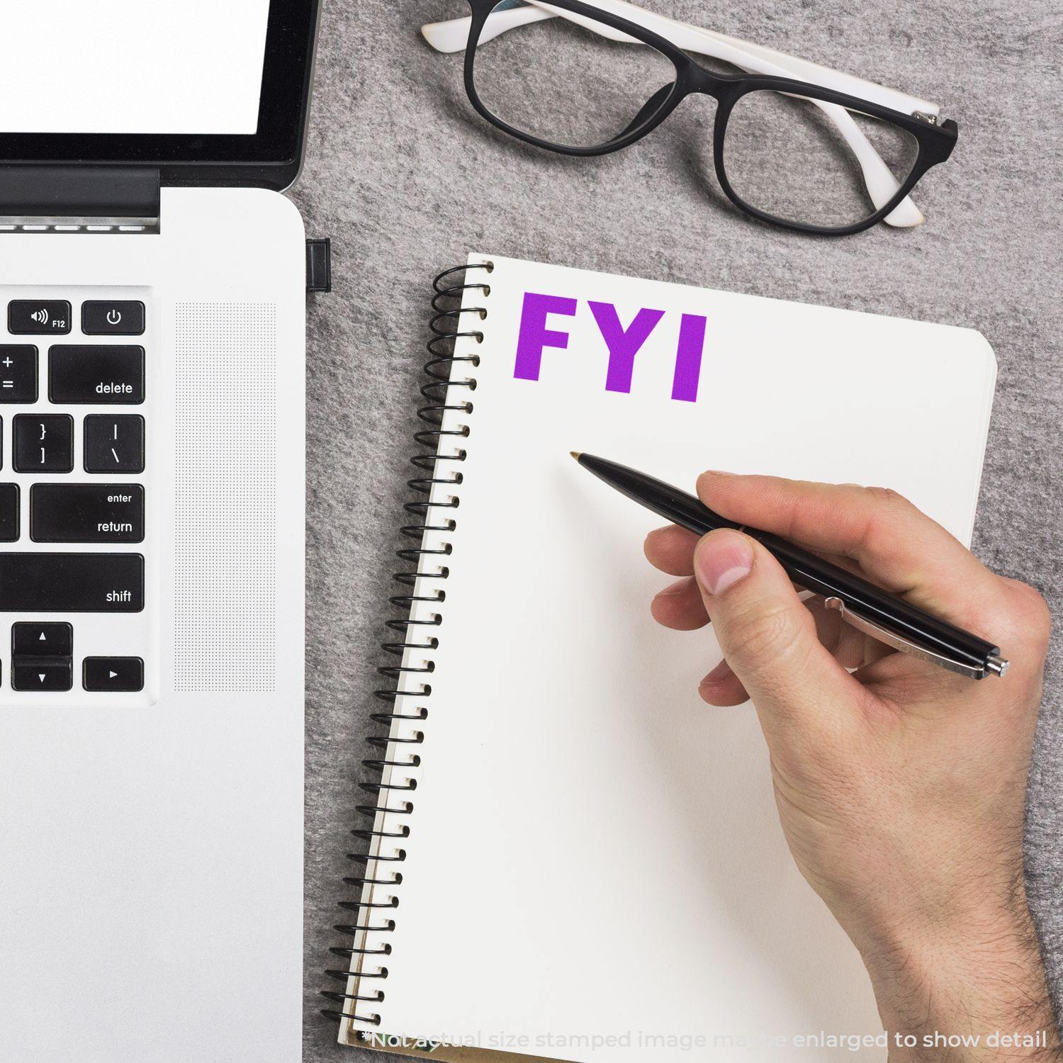 Person writing in a notebook stamped with "FYI" using the Large FYI Rubber Stamp, next to a laptop and glasses.