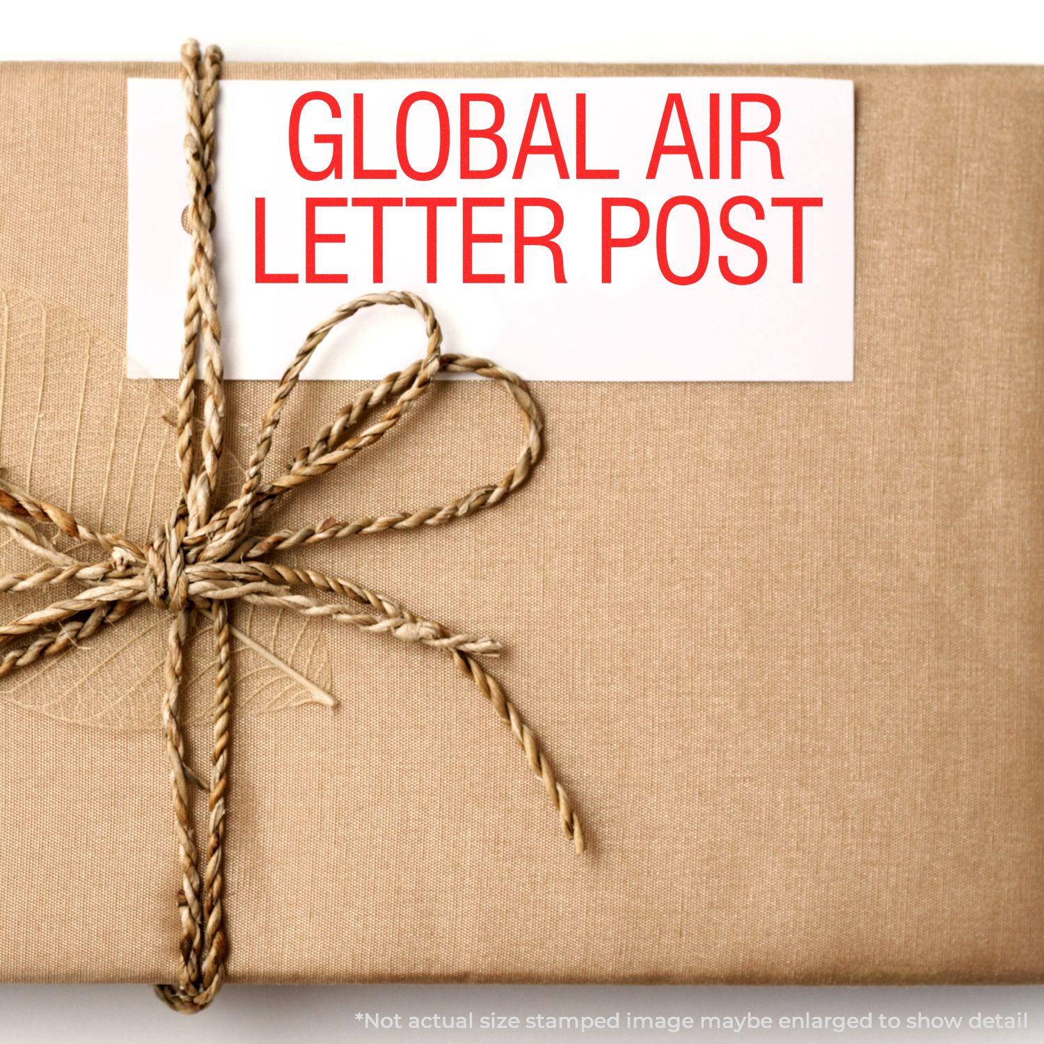 A wrapped package with a Large Self Inking Global Air Letter Post Stamp in red ink on a white label, tied with a brown twine bow.