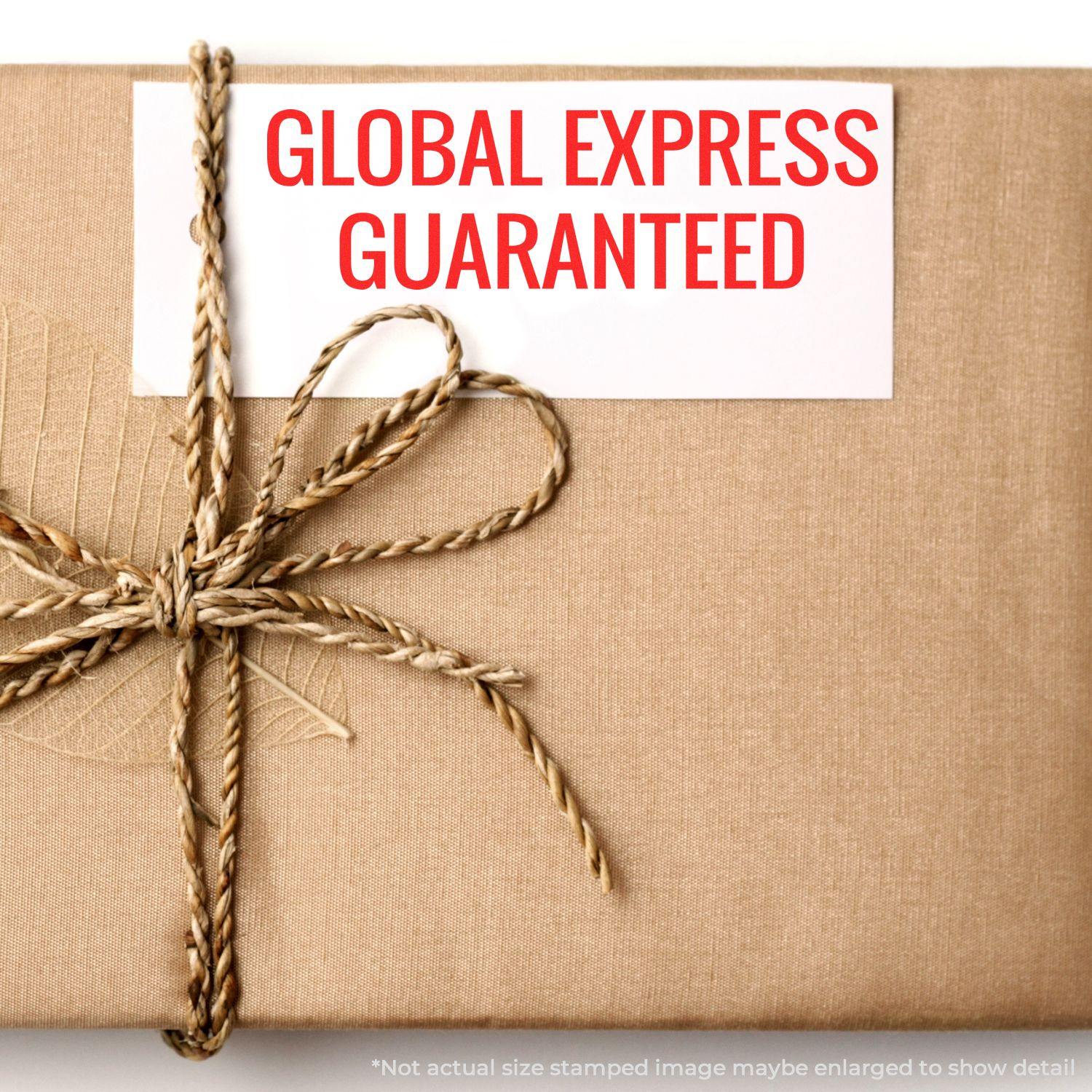 A Large Global Express Guaranteed Rubber Stamp is used on a white label attached to a brown wrapped package tied with twine.