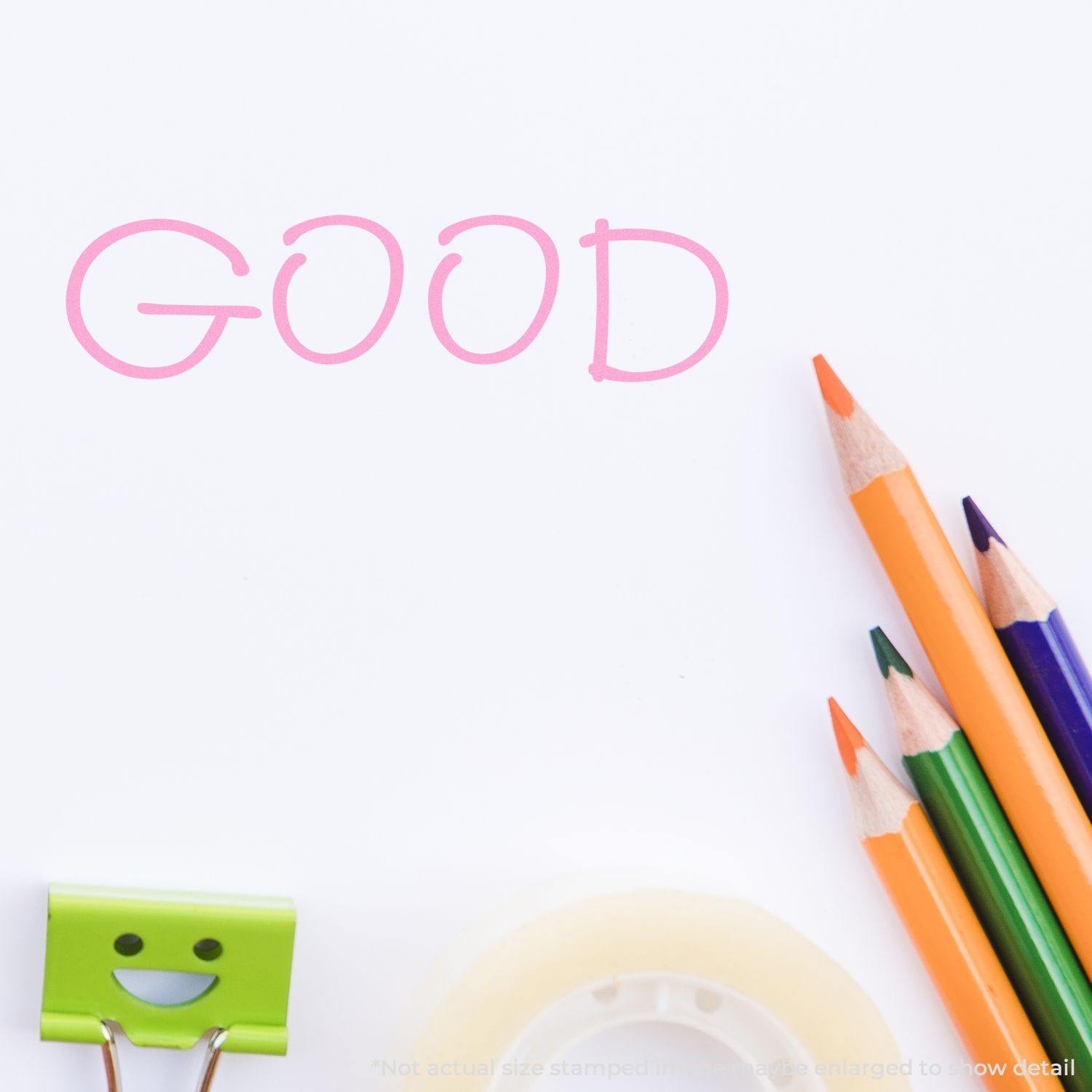 Good Rubber Stamp impression in pink on white paper, surrounded by colorful pencils, a smiling clip, and a roll of tape.