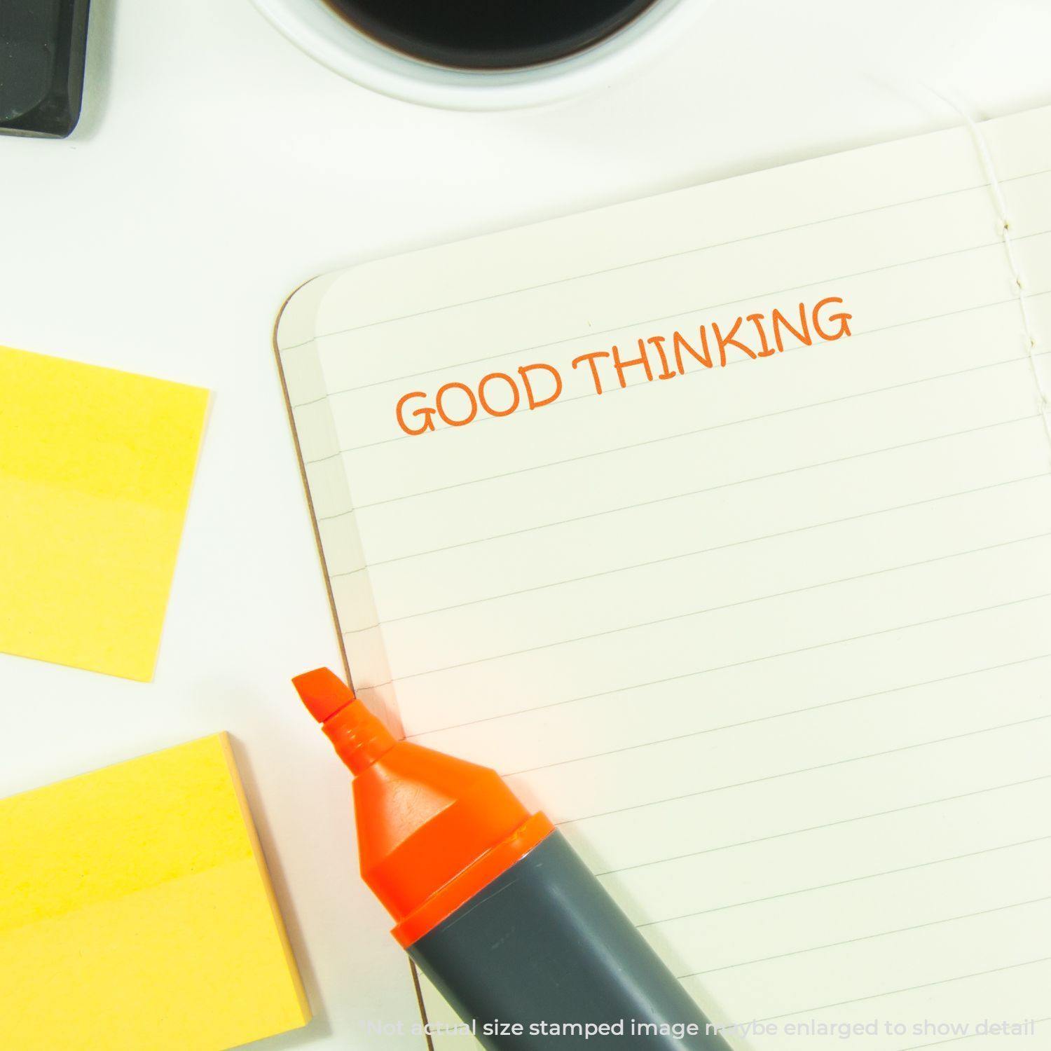 Slim Pre-Inked Good Thinking Stamp used on a notebook with orange ink, surrounded by sticky notes and an orange marker.