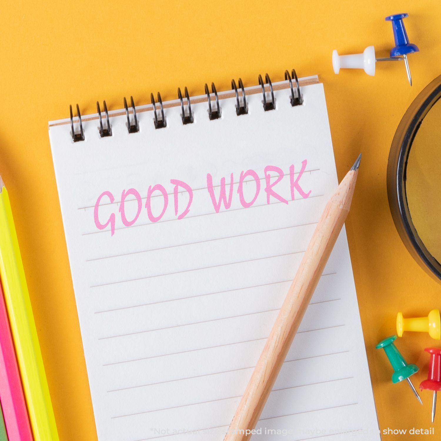 A notepad stamped with Good Work using the Good Work Rubber Stamp, surrounded by a pencil, push pins, and colorful stationery on a yellow background.