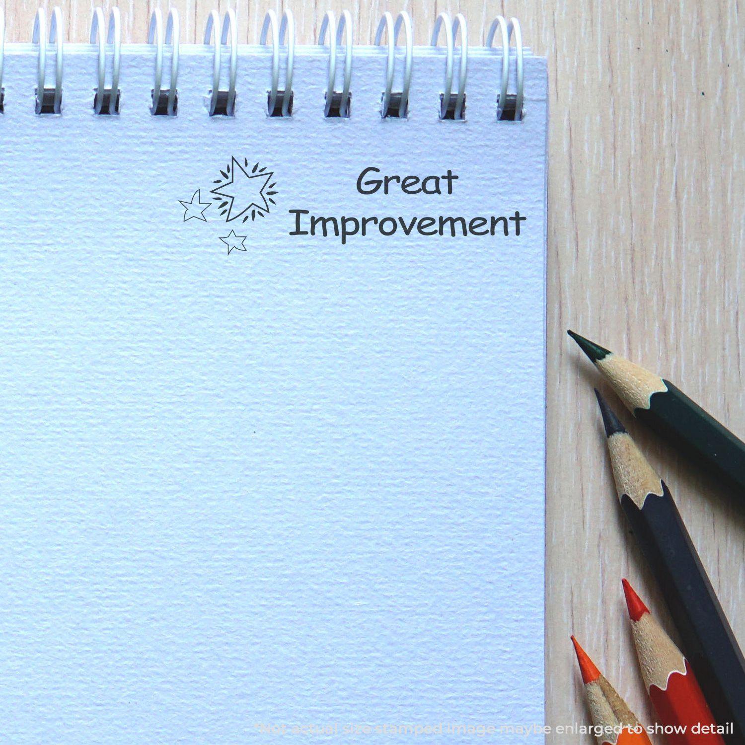 Slim Pre-Inked Great Improvement Stamp on a spiral notebook with colored pencils beside it on a wooden surface.