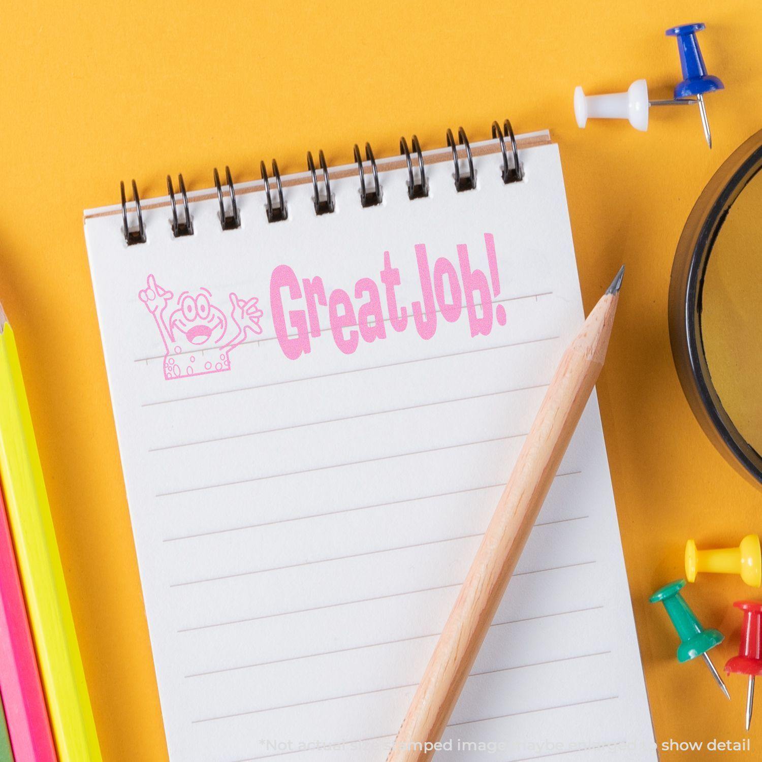 A Large Great Job Rubber Stamp imprint on a notepad with a pencil, colorful push pins, and highlighters on a yellow background.