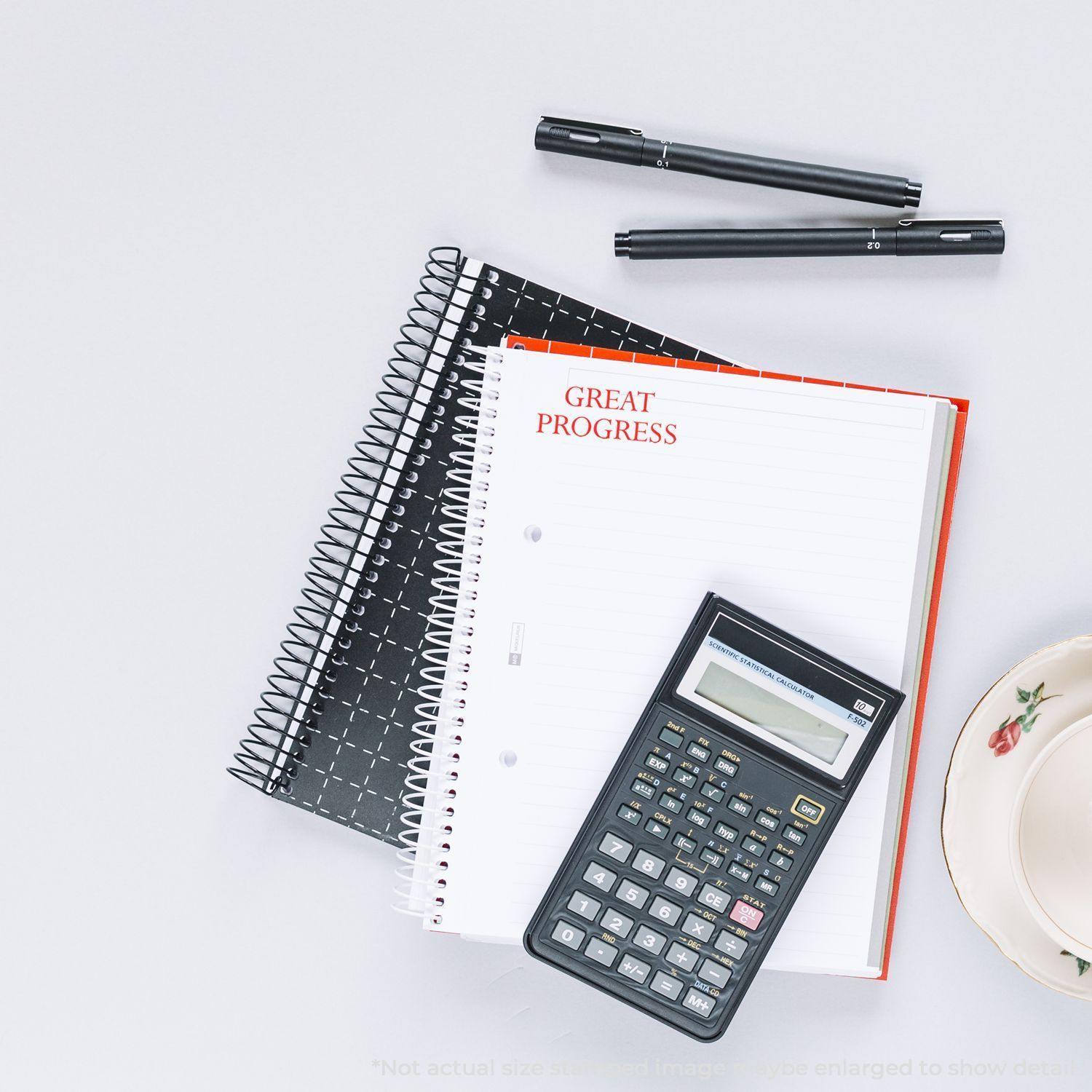 Notebook stamped with Great Progress Rubber Stamp beside a calculator, two pens, and a teacup on a white surface.