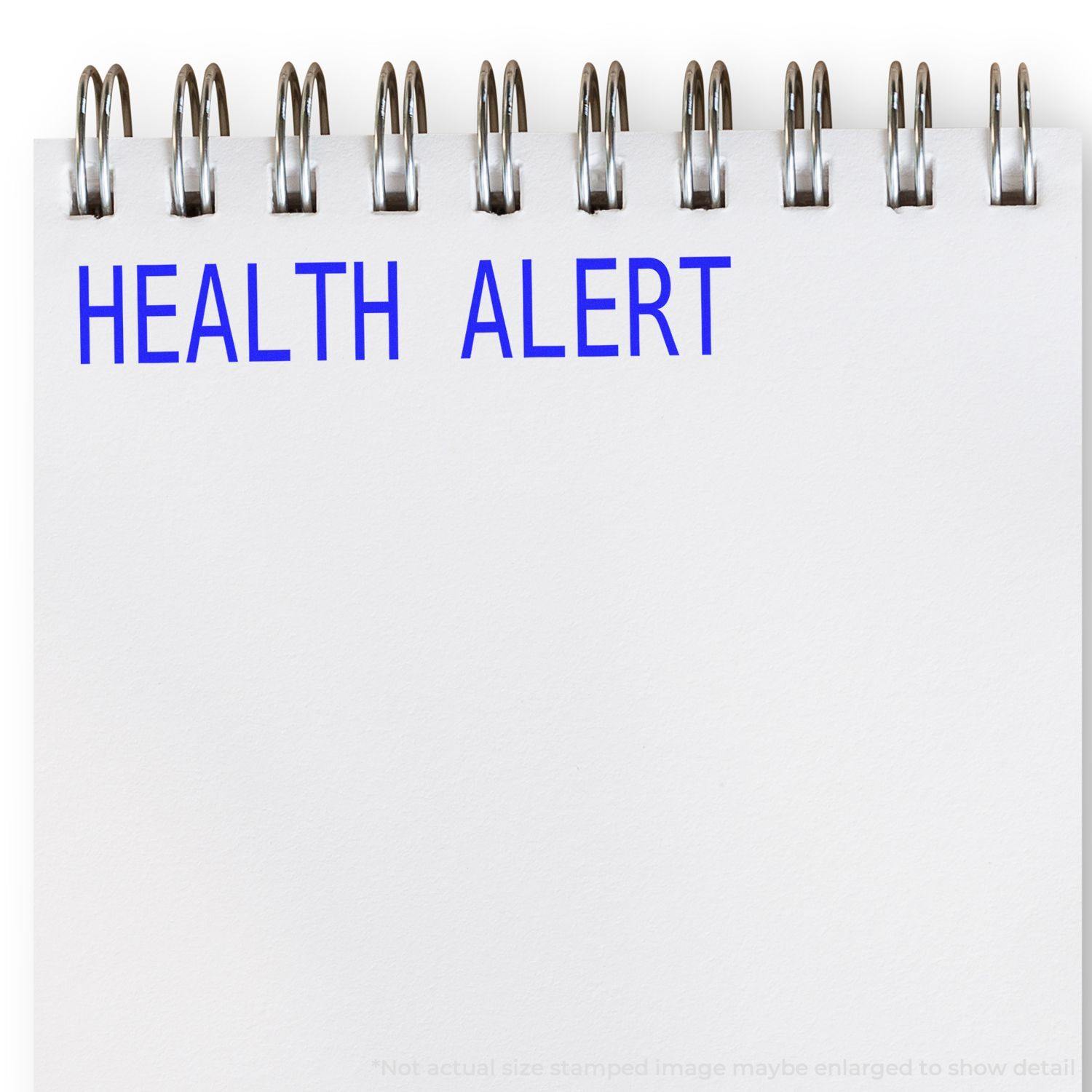 Health Alert Rubber Stamp in blue ink on a white spiral notebook, emphasizing the importance of health-related information.