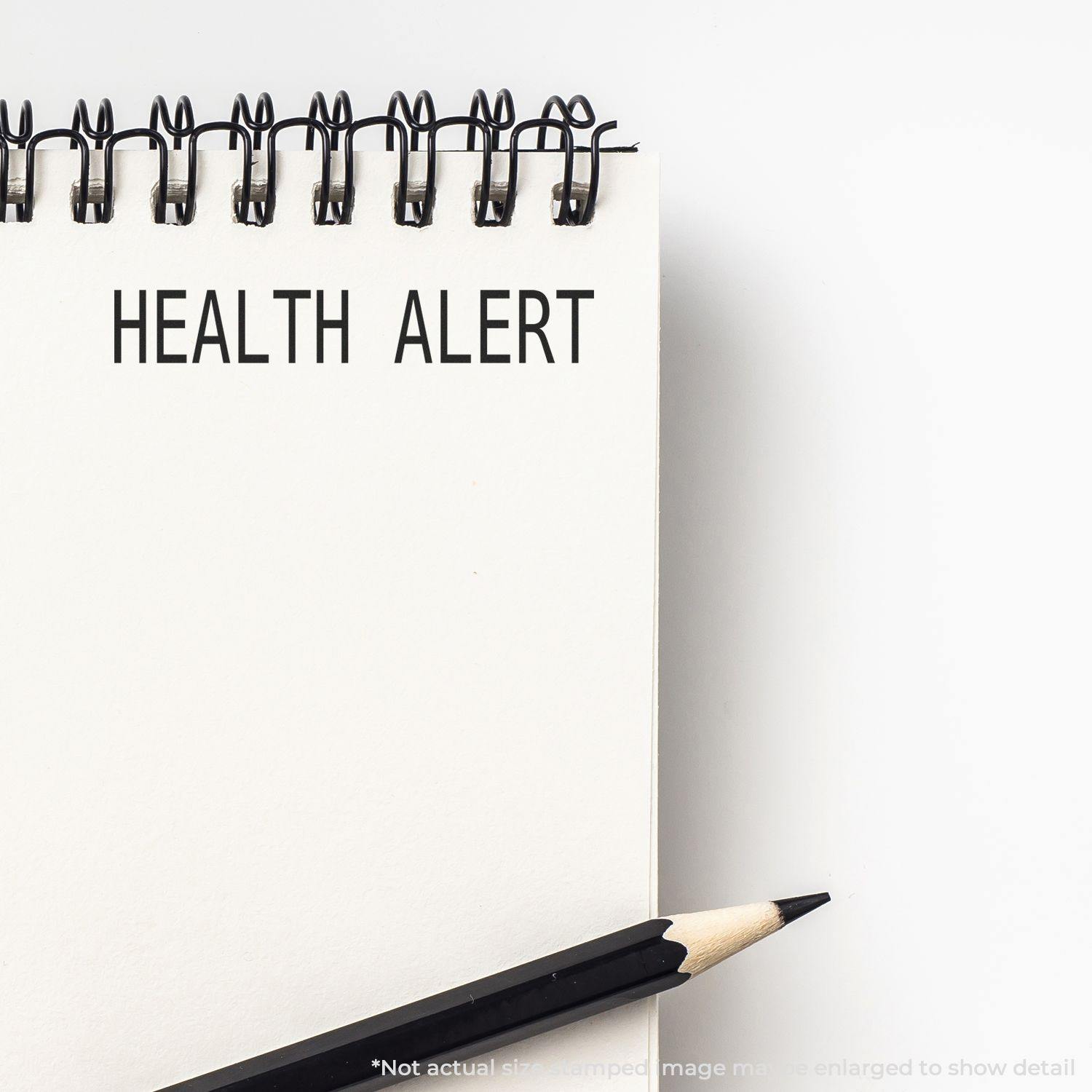 A notebook with Health Alert stamped on a page using the Health Alert Rubber Stamp, with a pencil placed beside the notebook.