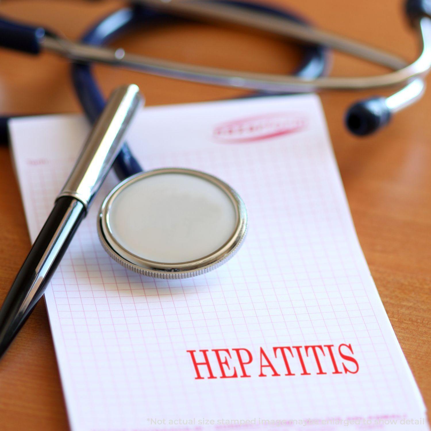 A Large Self Inking Hepatitis Stamp marks a paper with HEPATITIS in red ink, accompanied by a stethoscope and pen on a wooden desk.