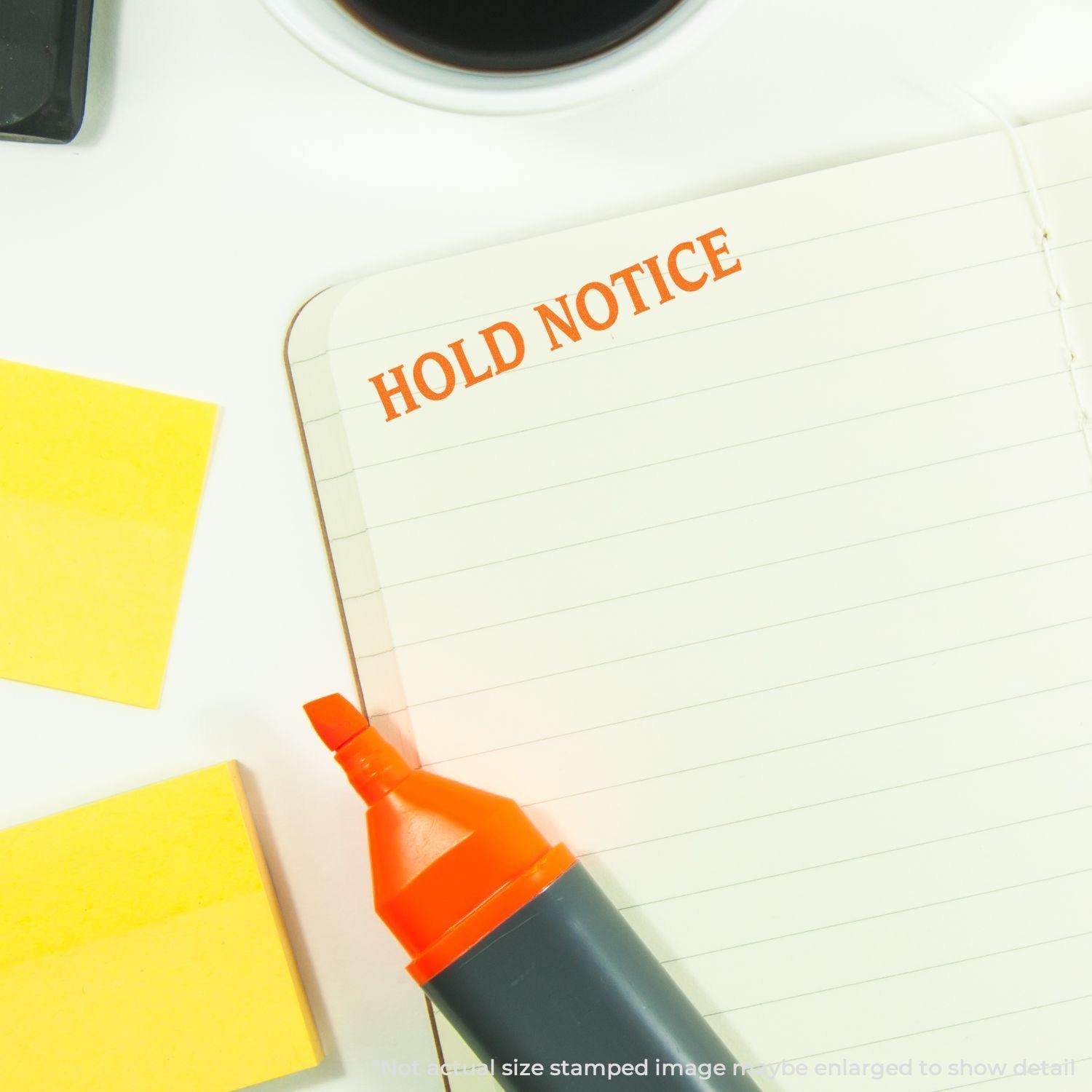 Large Hold Notice Rubber Stamp in use on a lined notebook, with a highlighter, sticky notes, and a coffee cup nearby.