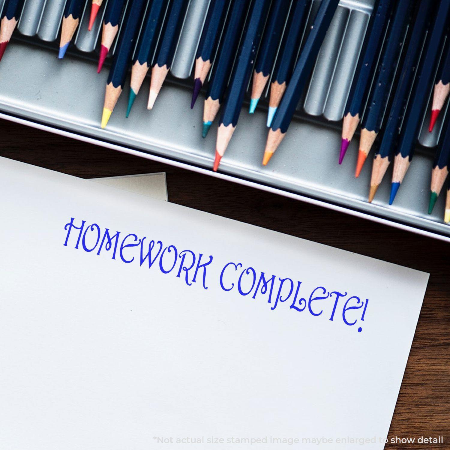 A Homework Complete Rubber Stamp impression on white paper, surrounded by colored pencils in a metal case.