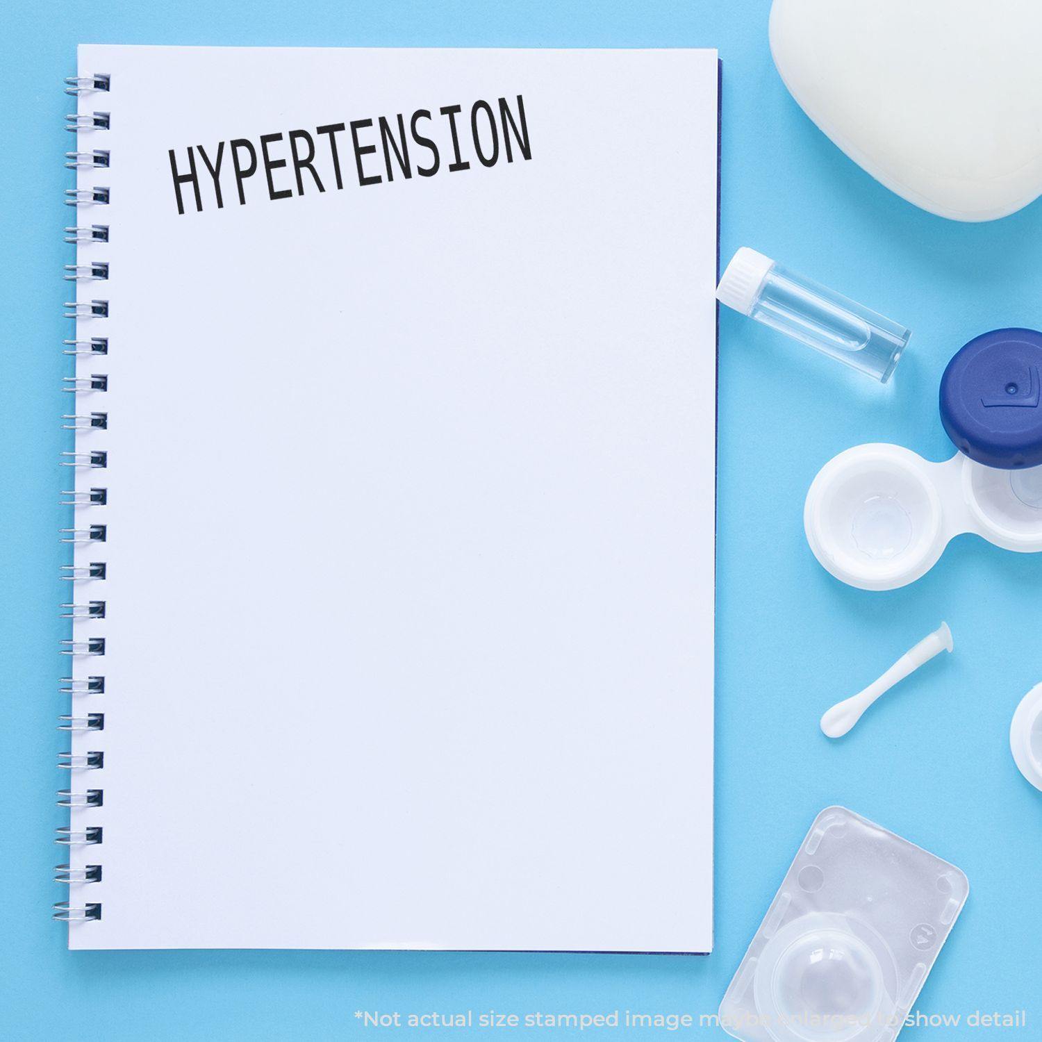 A notebook stamped with HYPERTENSION using the Large Pre-Inked Hypertension Stamp, surrounded by medical supplies on a blue background.