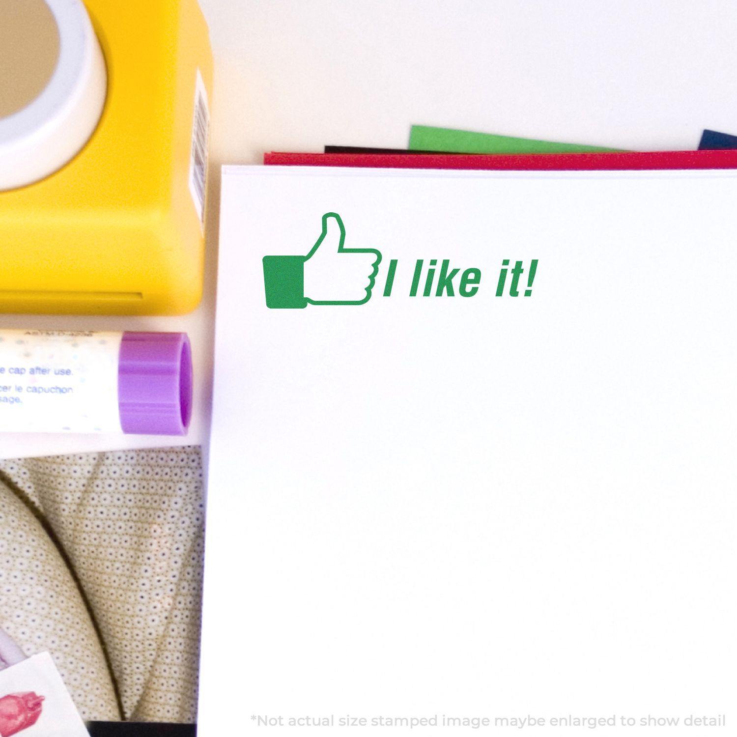 A paper stamped with the green Self Inking I like it Stamp featuring a thumbs-up icon, surrounded by office supplies.