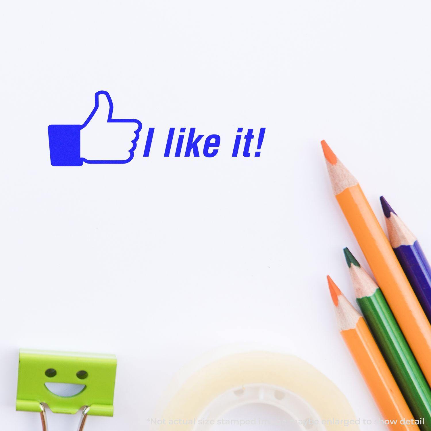 I like it Rubber Stamp impression with a thumbs-up icon, next to colorful pencils, a smiling binder clip, and a roll of tape on a white surface.