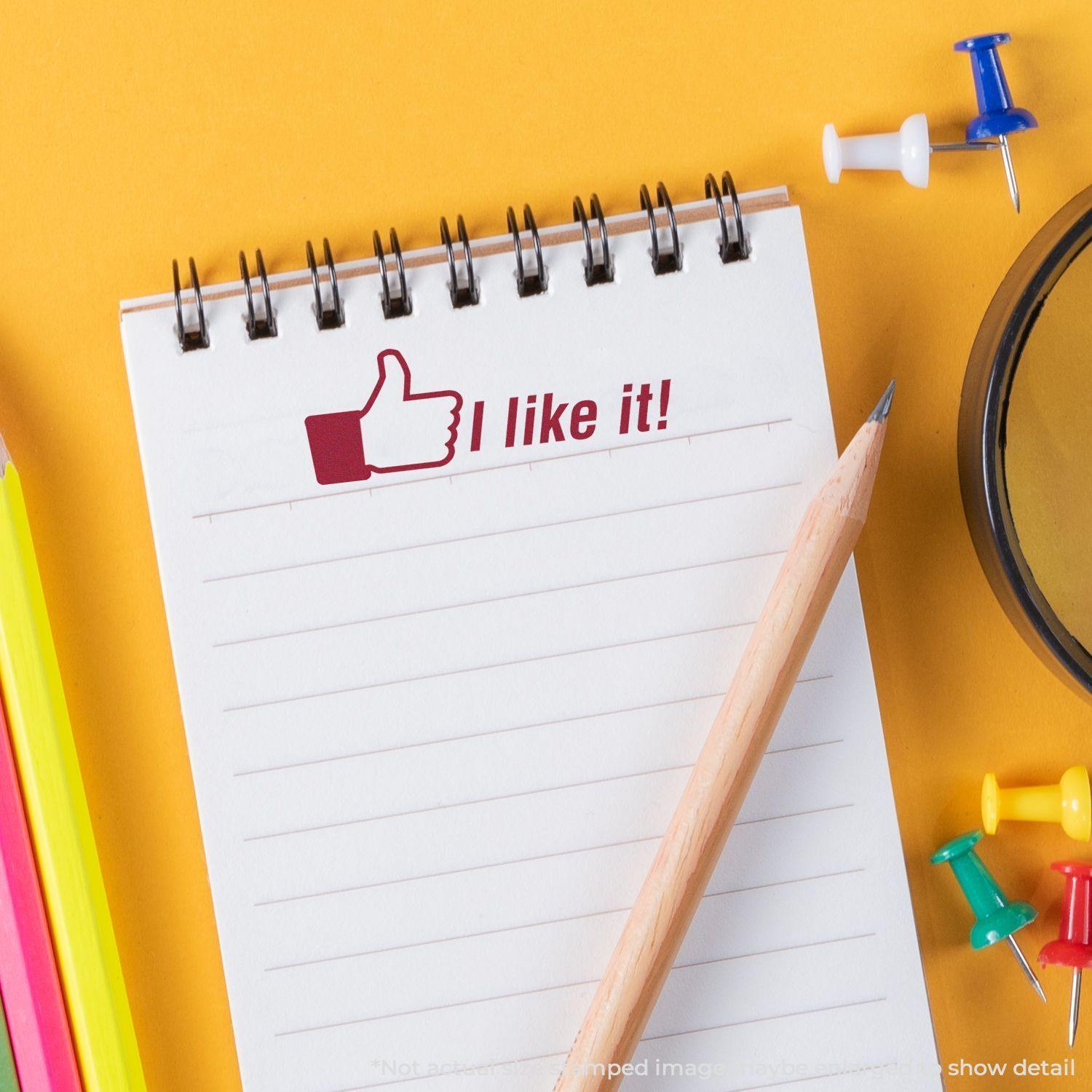 A Large I like it Rubber Stamp imprint on a notepad with a pencil, colorful push pins, and a magnifying glass on a yellow background.