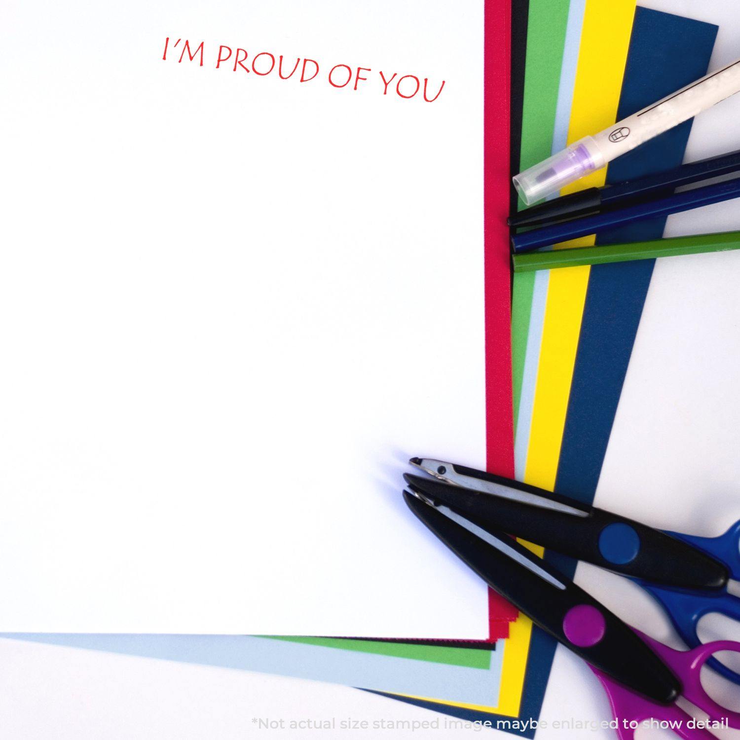 I'm Proud Of You Rubber Stamp used on white paper, surrounded by colorful sheets, scissors, and pens.