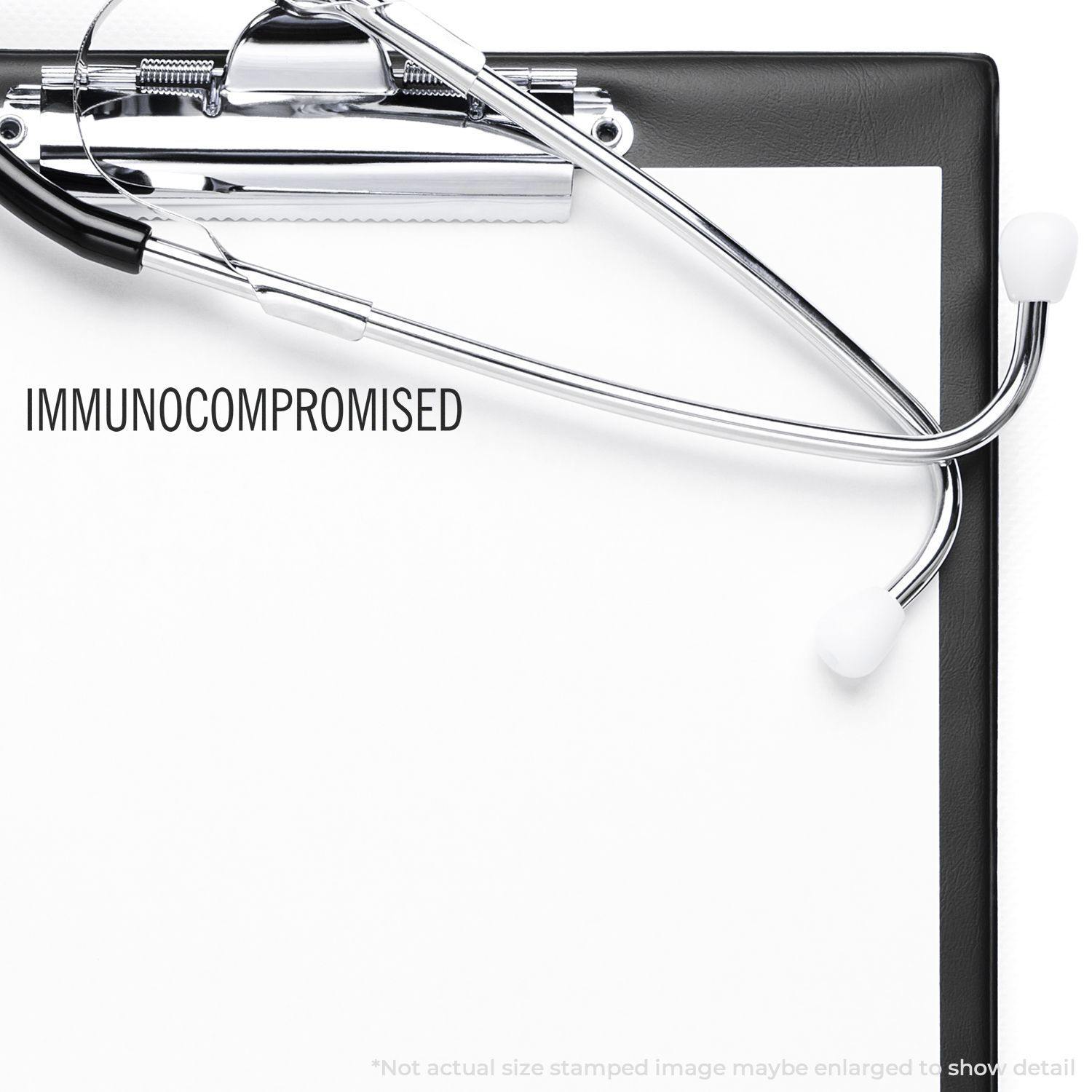 A self-inking stamp with a stamped image showing how the text "IMMUNOCOMPROMISED" in a large font is displayed by it after stamping.