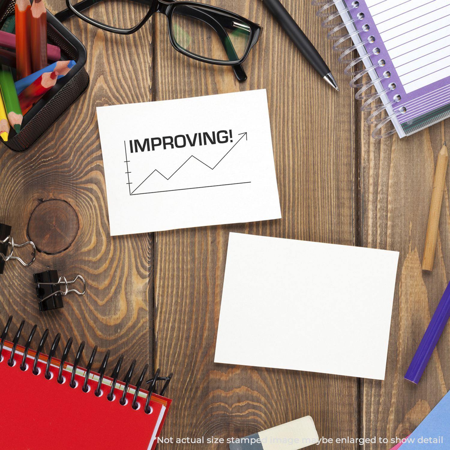 Desk with office supplies and a card stamped with Improving with Chart Icon Rubber Stamp showing an upward trend graph.