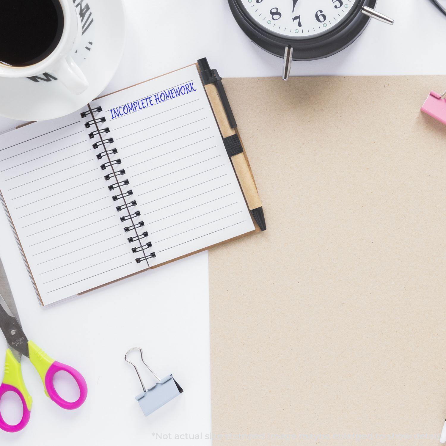 Self Inking Incomplete Homework Stamp used on an open notebook, surrounded by a clock, coffee mug, scissors, and other stationery items.