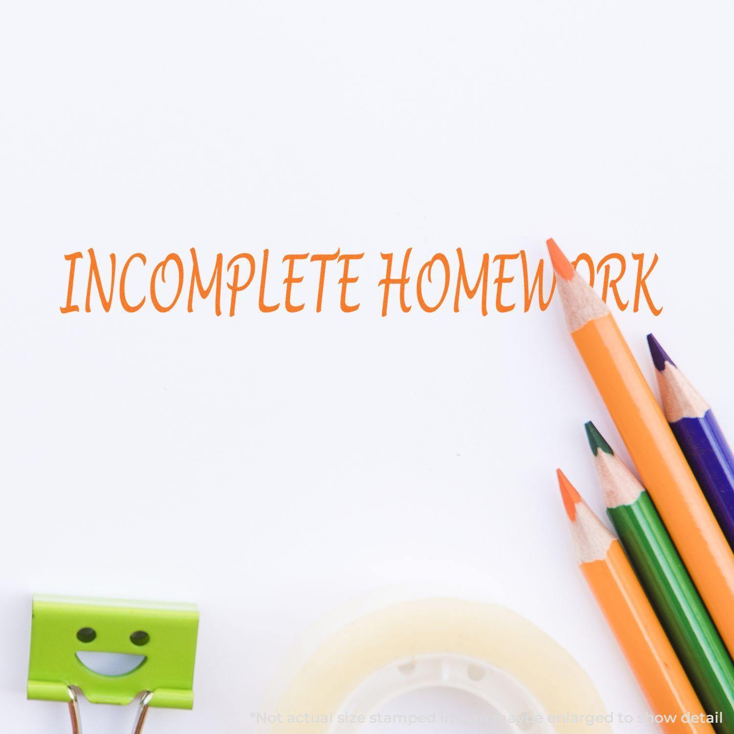 Large Incomplete Homework Rubber Stamp in use, with INCOMPLETE HOMEWORK stamped in orange, surrounded by pencils, tape, and a smiling clip.