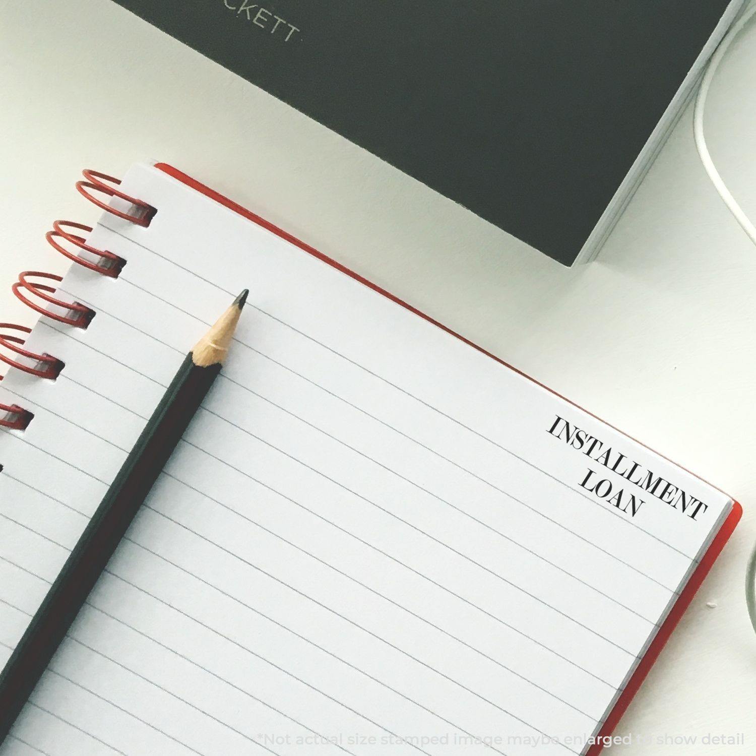 A Self Inking Installment Loan Stamp is used on a lined notepad with a pencil beside it.