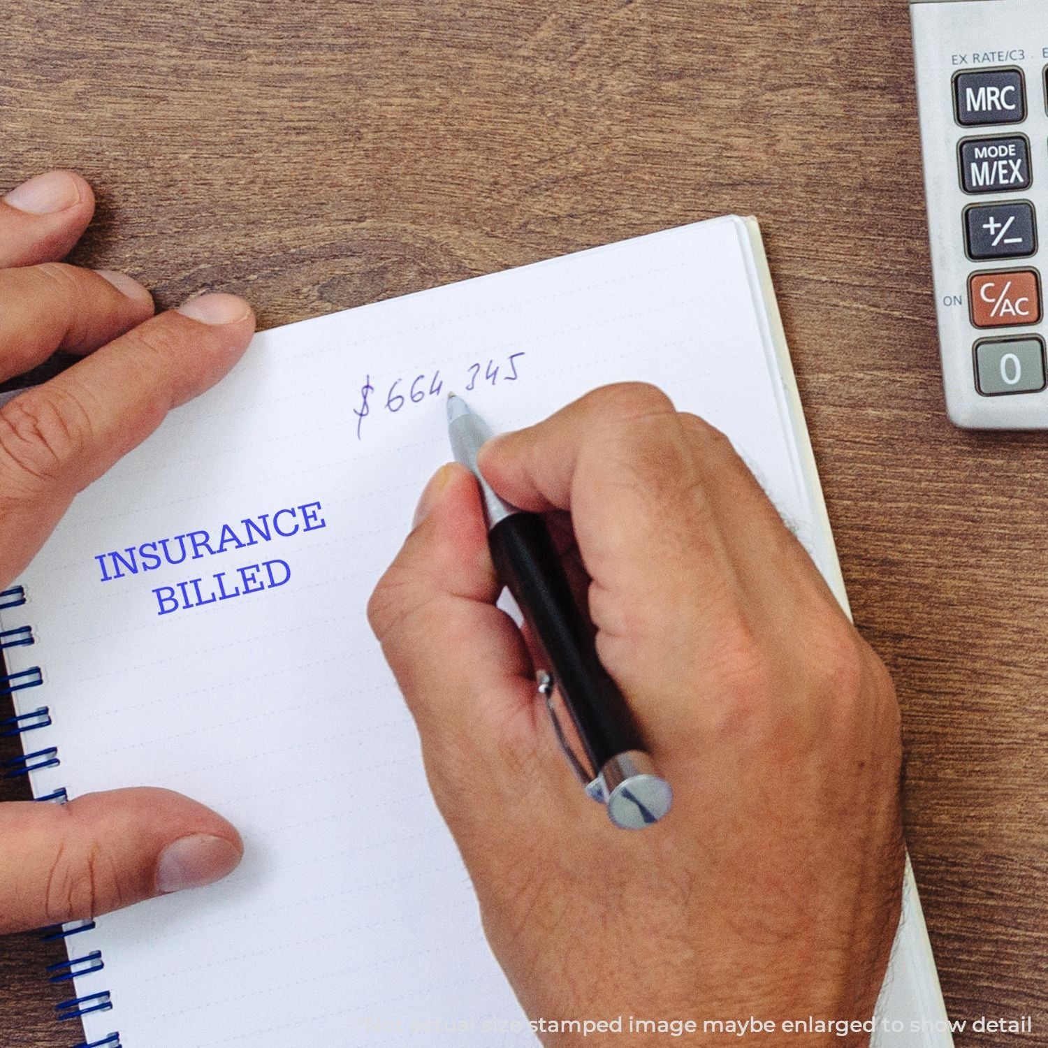 A hand writing in a notebook with INSURANCE BILLED stamped using a Self Inking Insurance Billed Stamp, next to a calculator on a wooden desk.