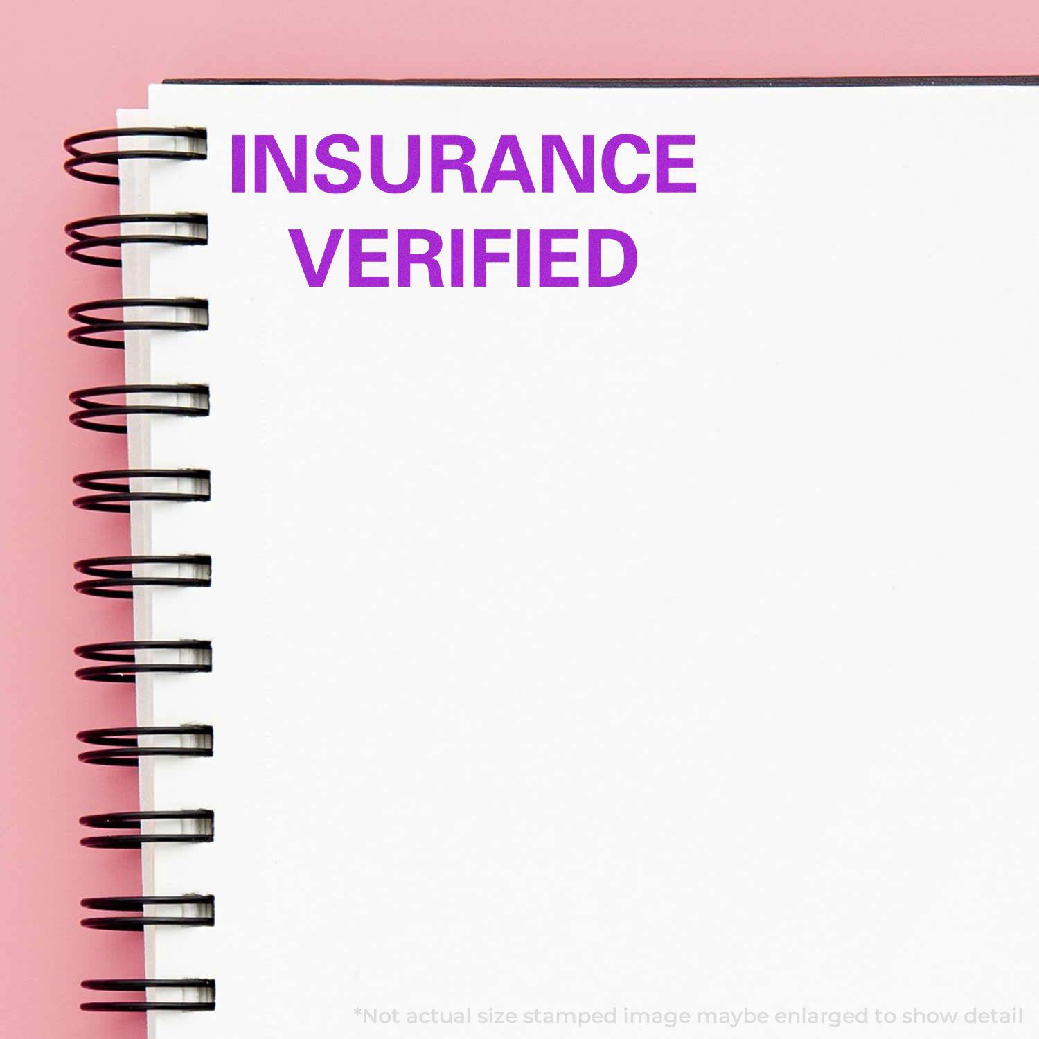 Insurance Verified Rubber Stamp imprint on a white spiral notebook with a pink background.