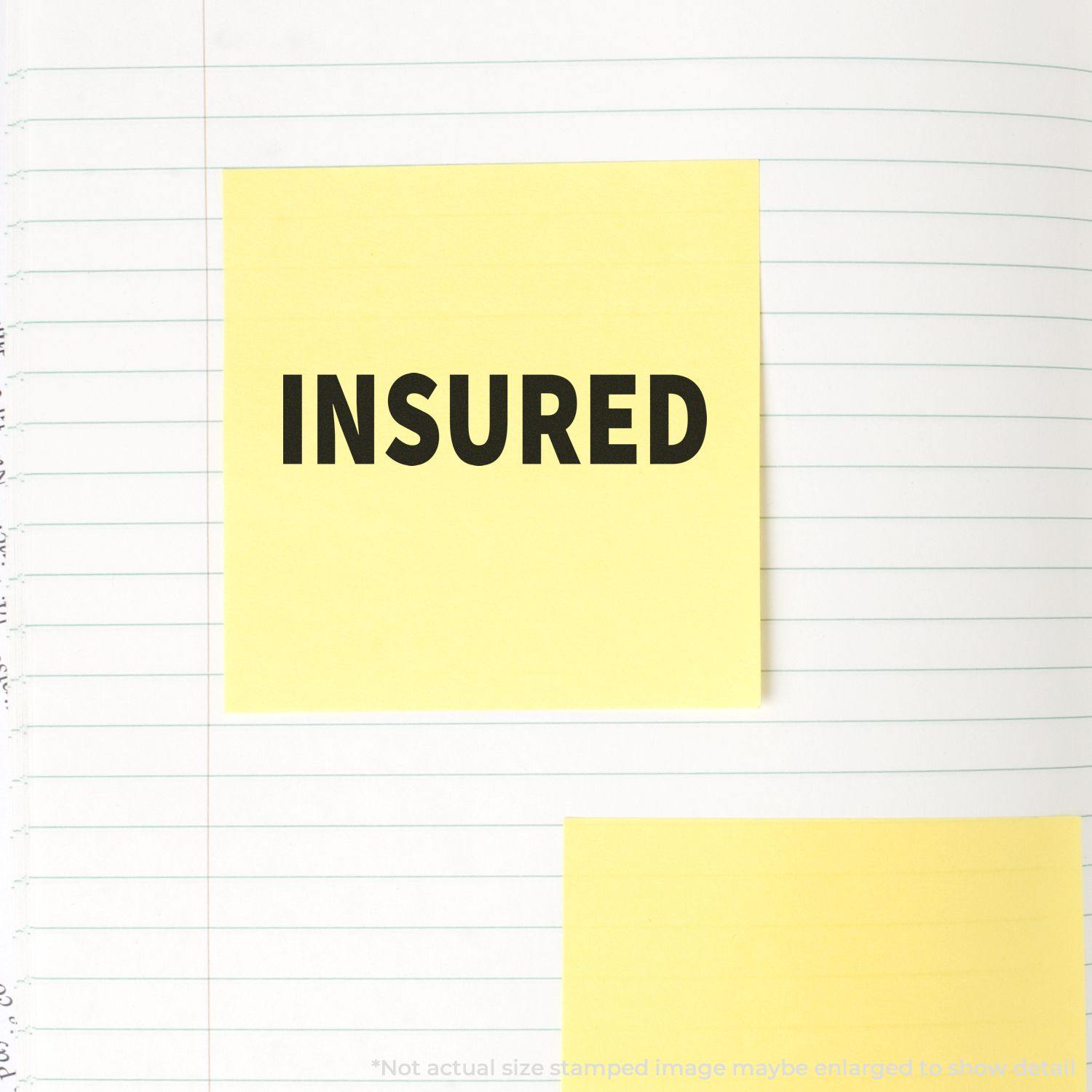 Insured Rubber Stamp used on a yellow sticky note placed on a lined notebook page. The word INSURED is clearly visible in bold black letters.