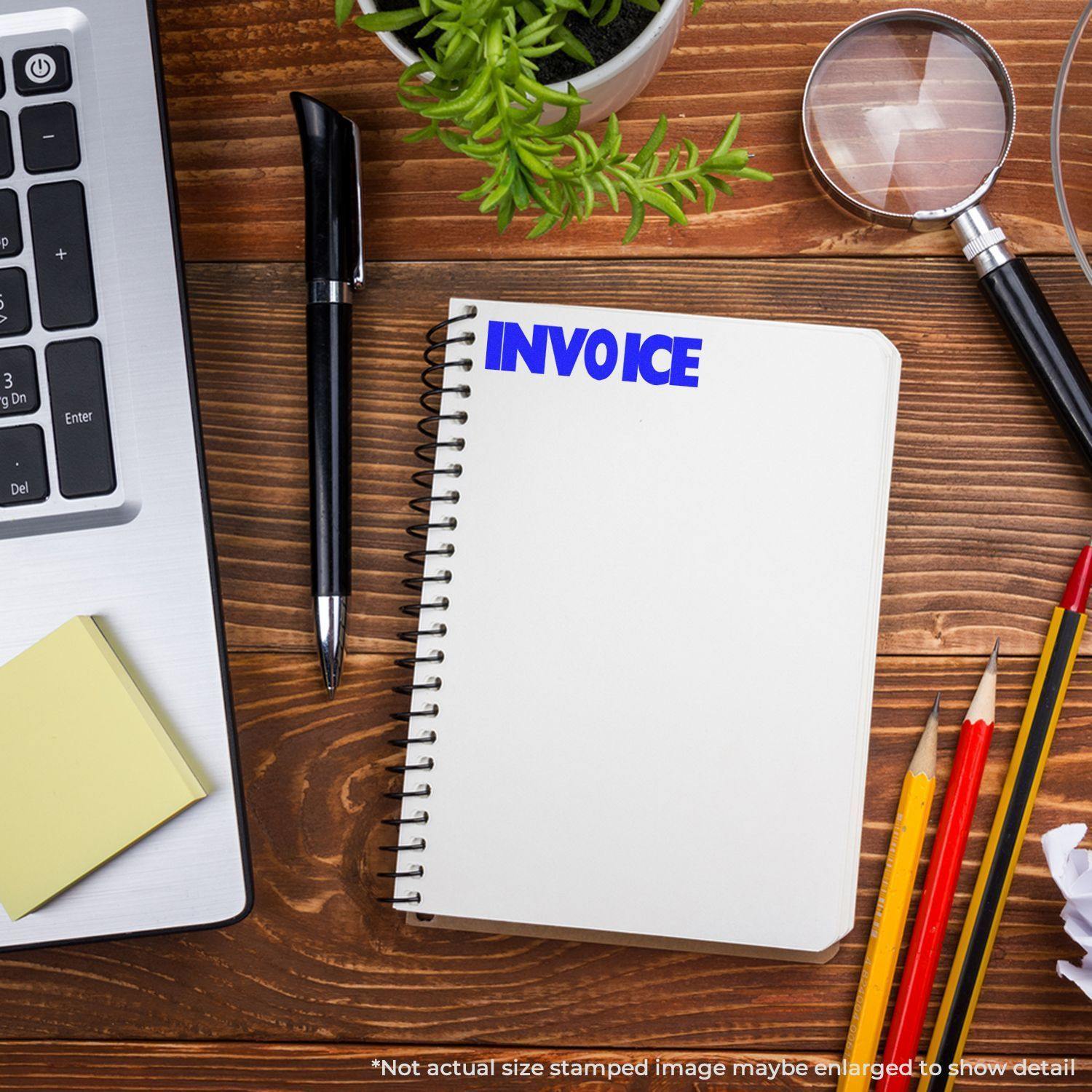 Invoice Rubber Stamp used on a notebook, placed on a wooden desk with a laptop, pen, sticky notes, magnifying glass, and pencils.