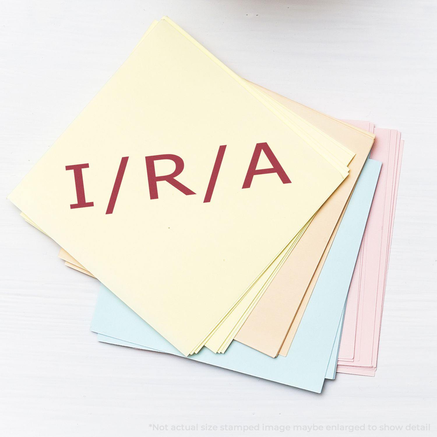 A stack of pastel-colored papers with I/R/A stamped in red using the I/R/A Rubber Stamp, showcasing the stamp's clear and bold imprint.