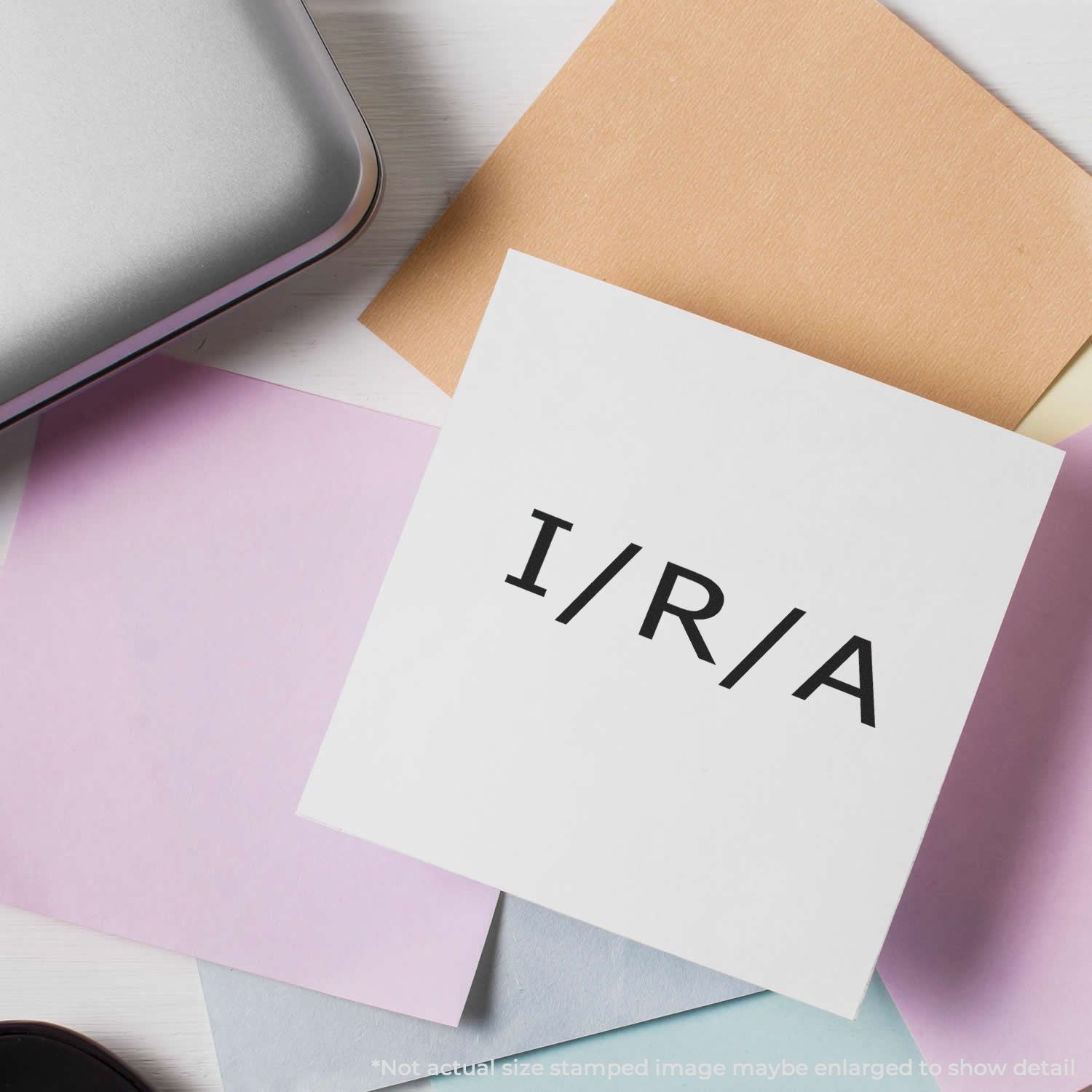 Self Inking Ira Stamp in use on a white paper with I/R/A text, surrounded by pastel-colored papers and a silver laptop.