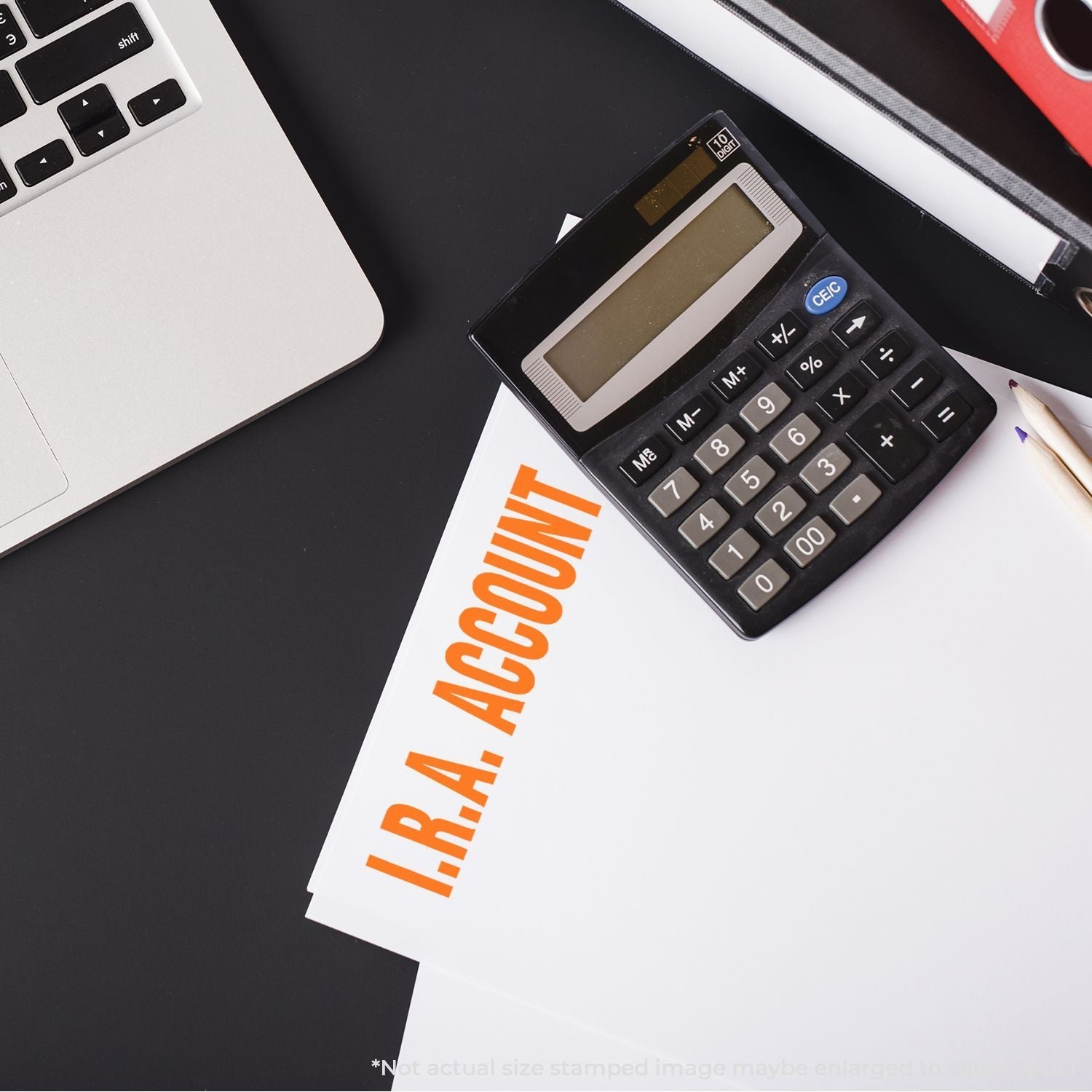 Self Inking IRA Account Stamp used on a document next to a calculator, pencil, and laptop on a black desk.