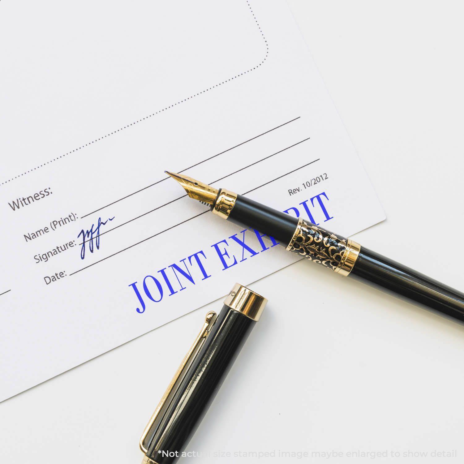 Large Self Inking Joint Exhibit Stamp marking a document with JOINT EXHIBIT in blue ink, alongside a black and gold fountain pen.