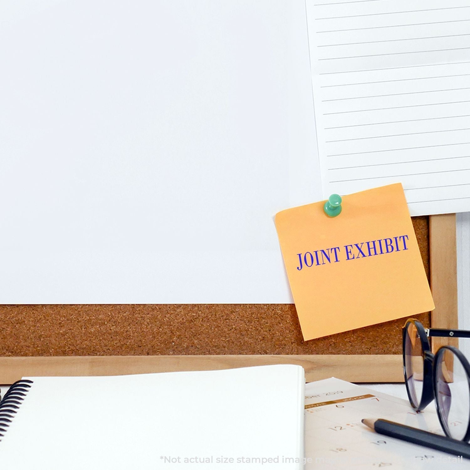 Self Inking Joint Exhibit Stamp used on a yellow sticky note pinned to a corkboard, with a notebook, glasses, and papers nearby.