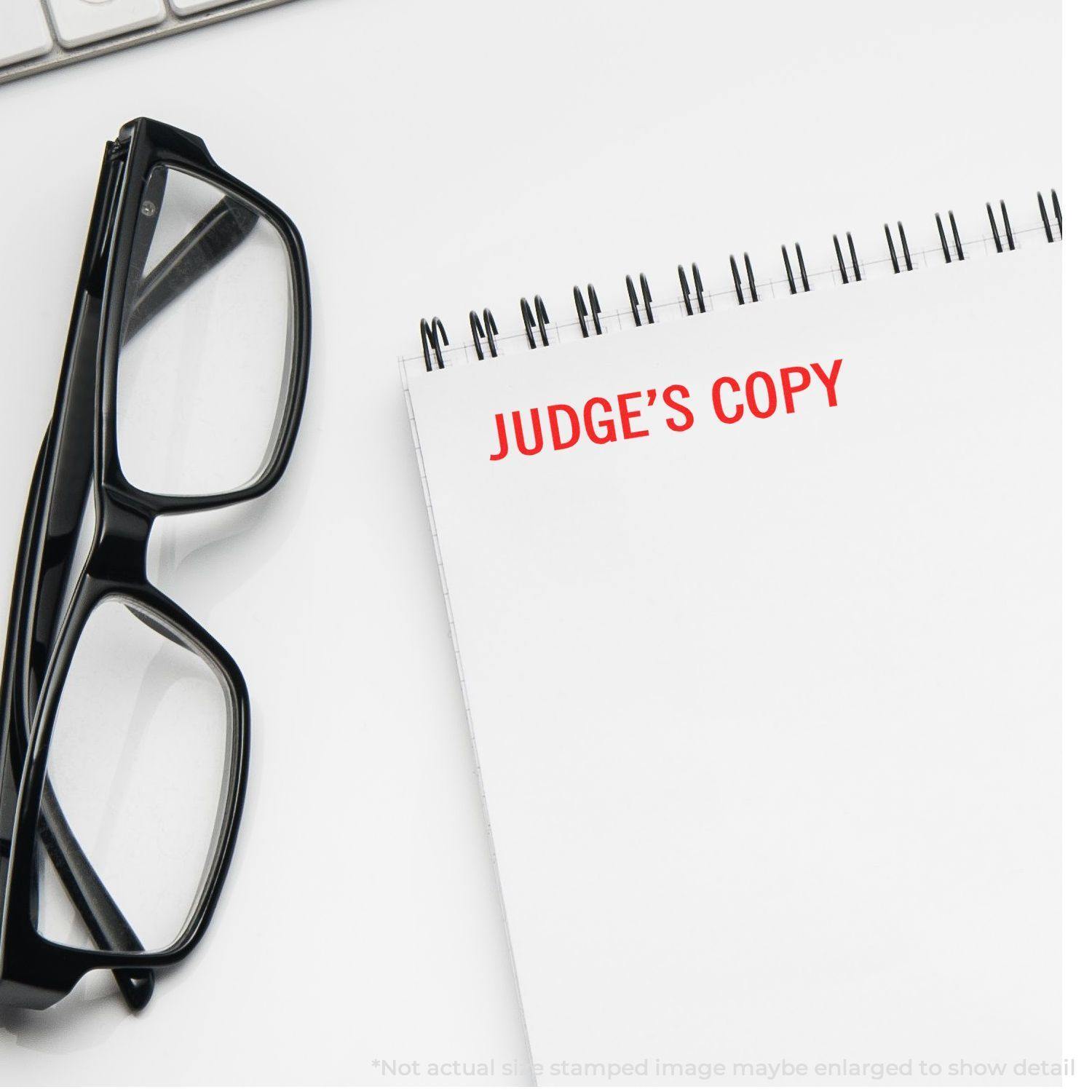 A pair of glasses and a notepad with JUDGE'S COPY stamped in red using the Large Self Inking Judge's Copy Stamp.