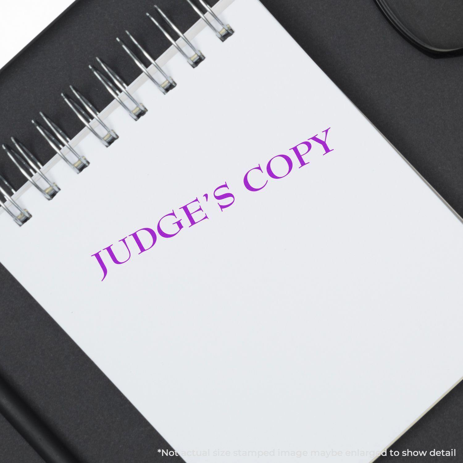 A notebook with JUDGE'S COPY stamped in purple using the Judges Copy Legal Rubber Stamp, placed on a black surface.