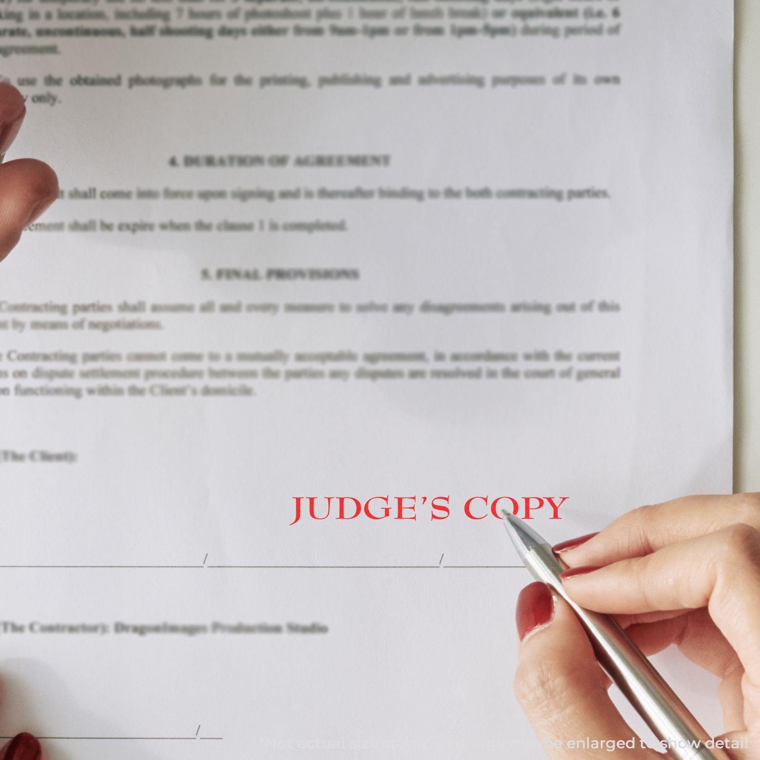 A hand holding a pen near a document stamped with JUDGE'S COPY in red using the Judges Copy Legal Rubber Stamp.