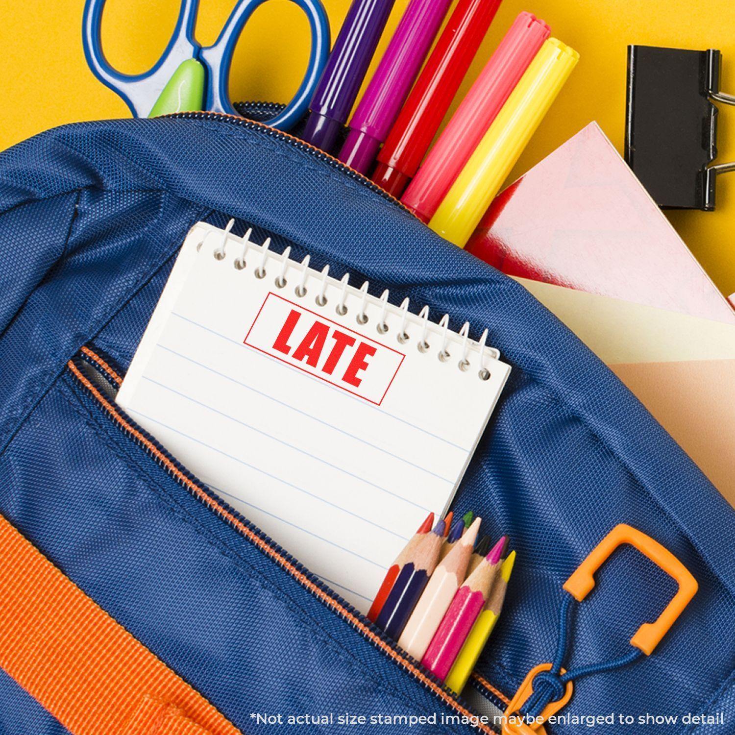 Slim Pre-Inked Late with Border Stamp on a notebook in a blue backpack with colored pencils, scissors, and markers.