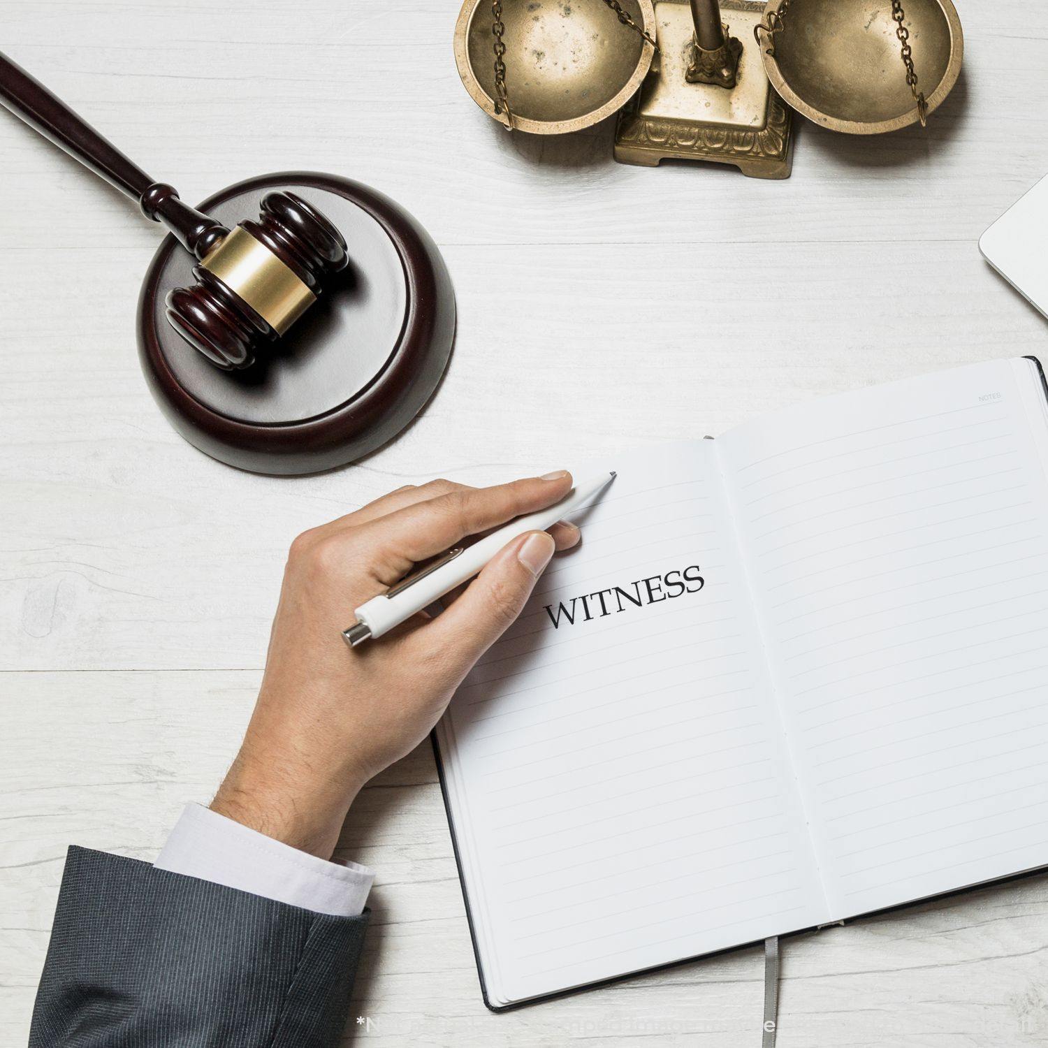 A hand holding a pen writes WITNESS in a notebook, with a gavel and scales of justice nearby, representing a Legal Witness Rubber Stamp.