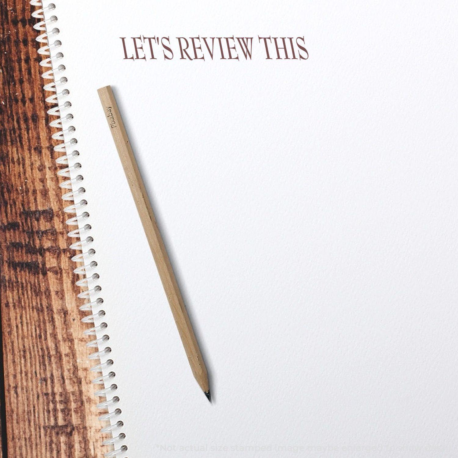 A Large Self Inking Lets Review This Stamp imprint on a white spiral notebook page with a wooden pencil placed beside it.