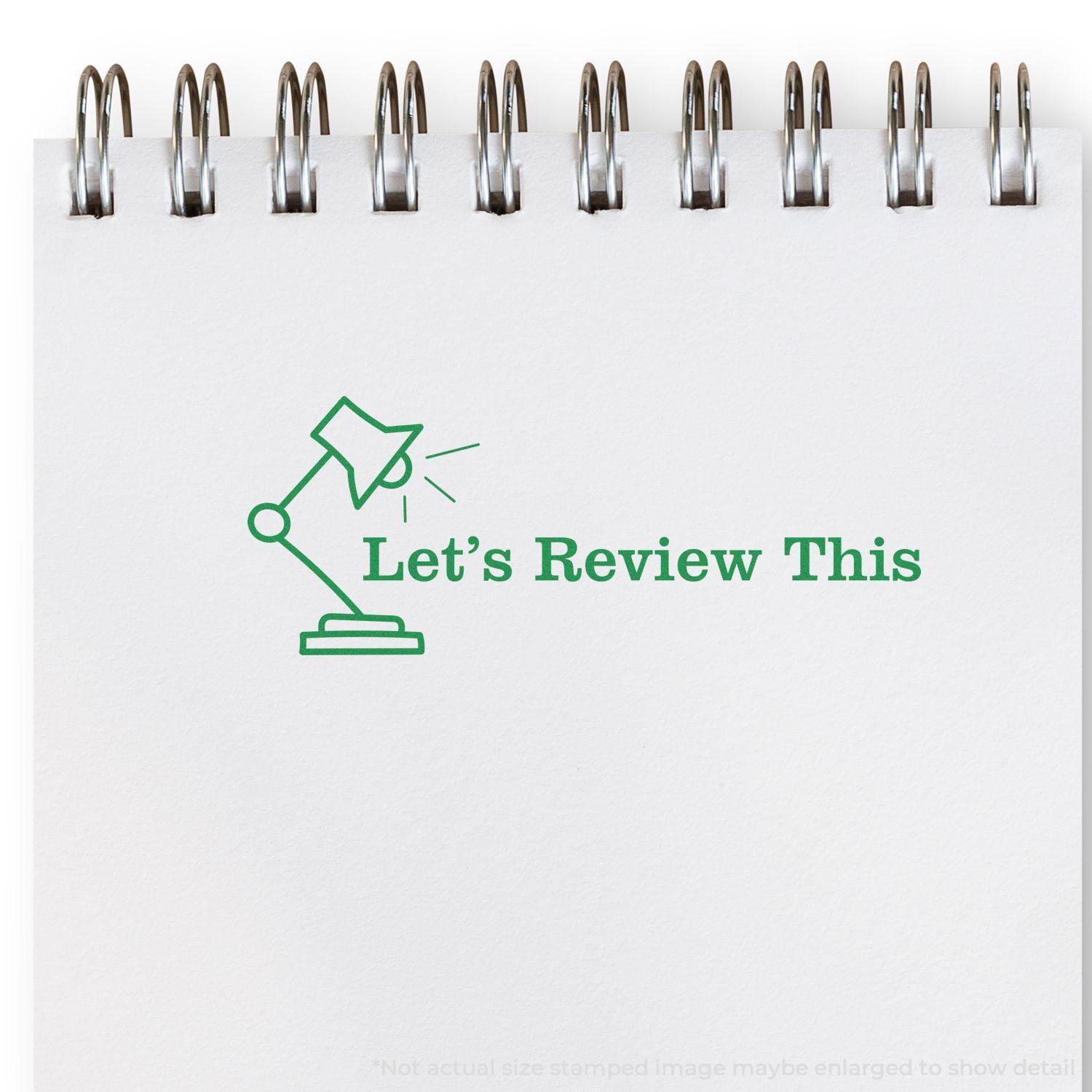 A stock office rubber stamp with a stamped image showing how the text "Let's Review This" in a large bold font with the image of a lamp is displayed after stamping.