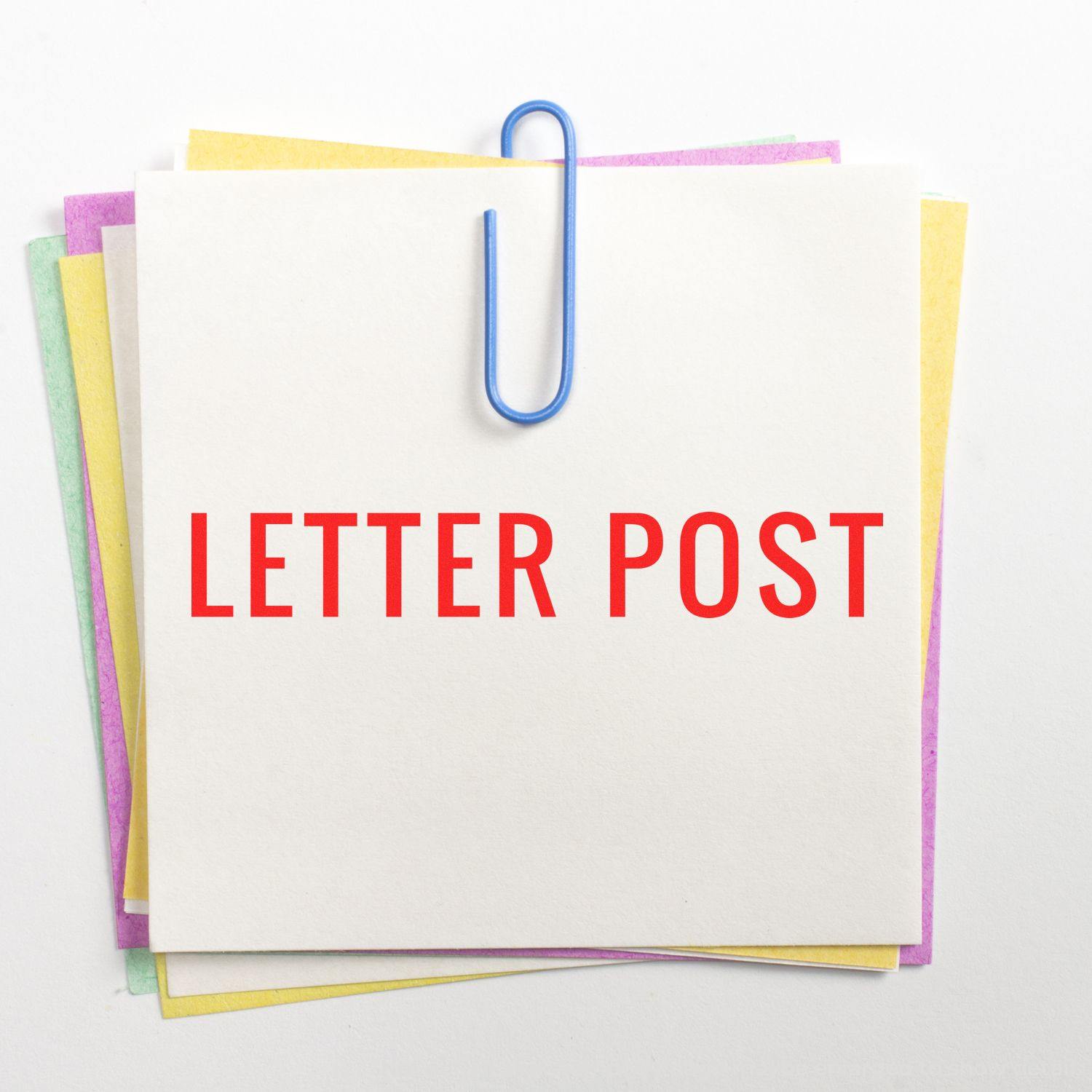 A stack of colorful papers with a blue paperclip holding a white sheet stamped with LETTER POST using a Slim Pre-Inked Letter Post Stamp.