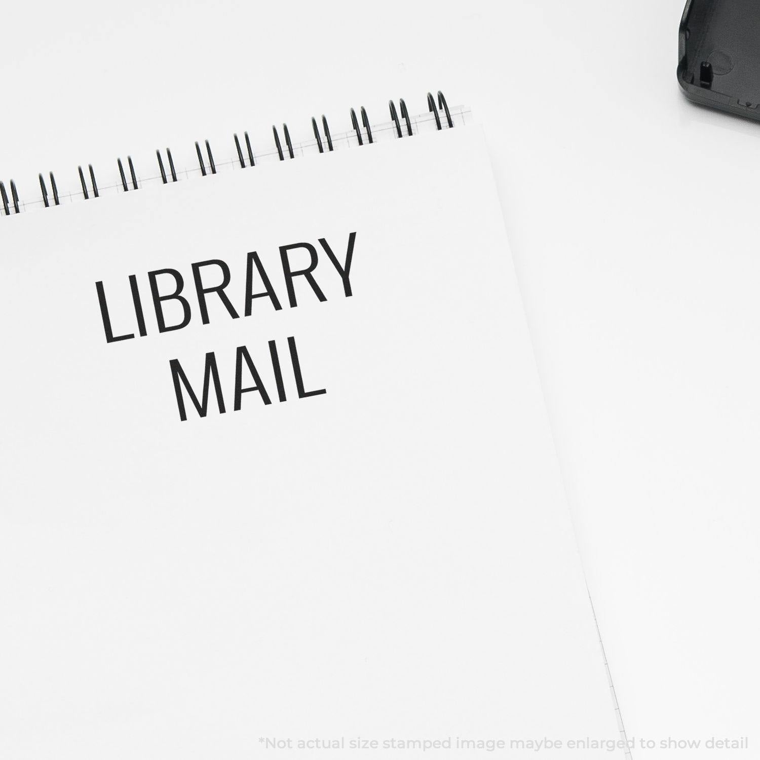 Library Mail rubber stamp impression on a white spiral notebook, with a black stamp device partially visible in the corner.