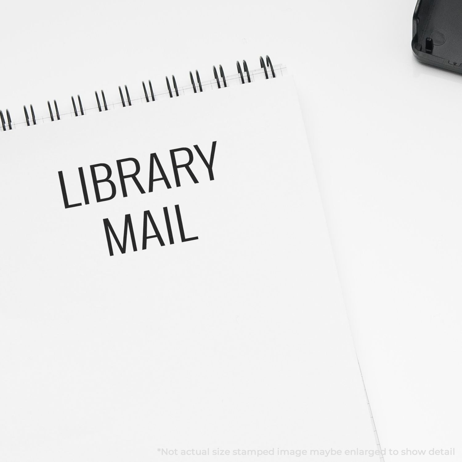 Self Inking Library Mail Stamp imprint on a white notepad, with the stamp device partially visible in the top right corner.