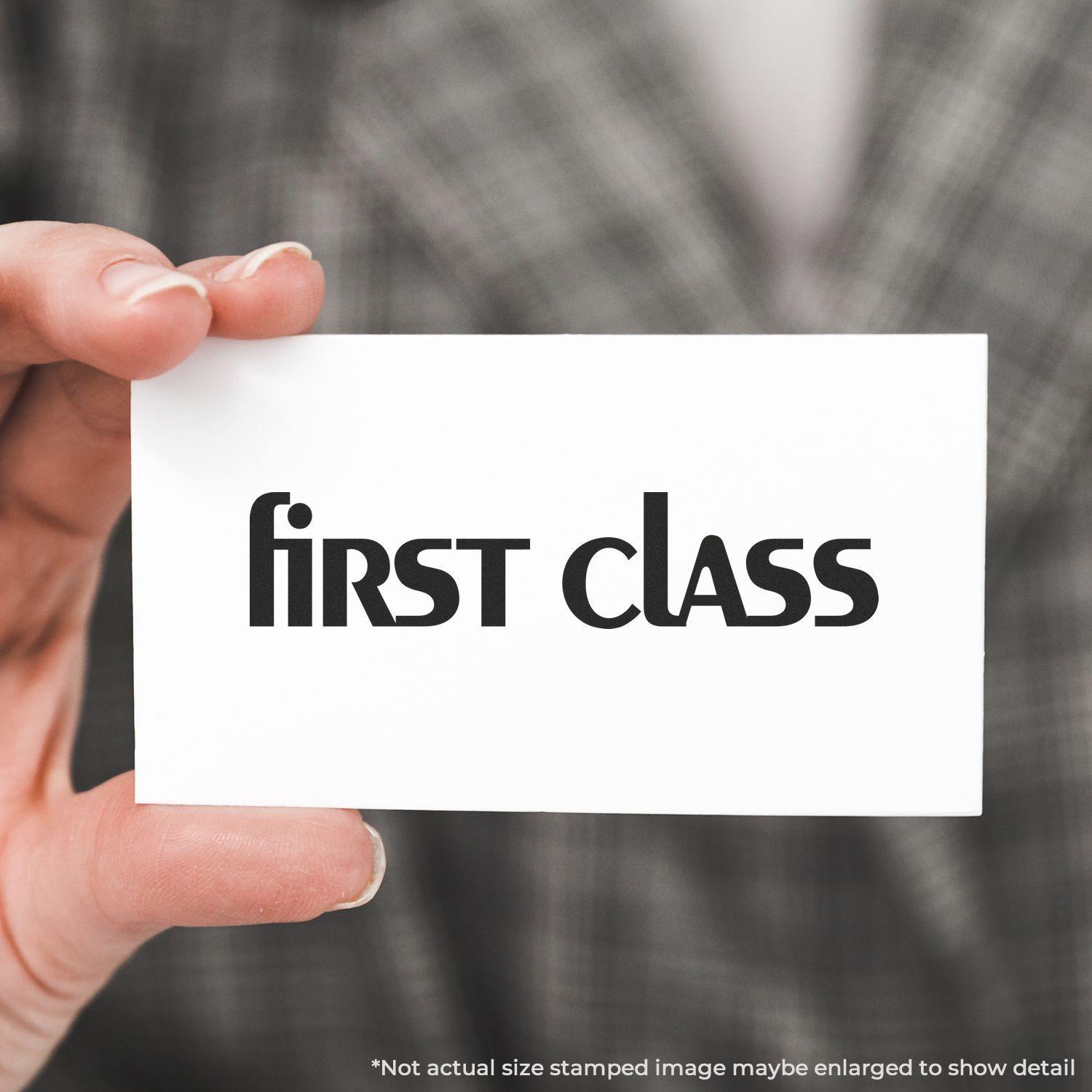 Person holding a card with first class stamped in lower case using a rubber stamp, wearing a plaid jacket in the background.