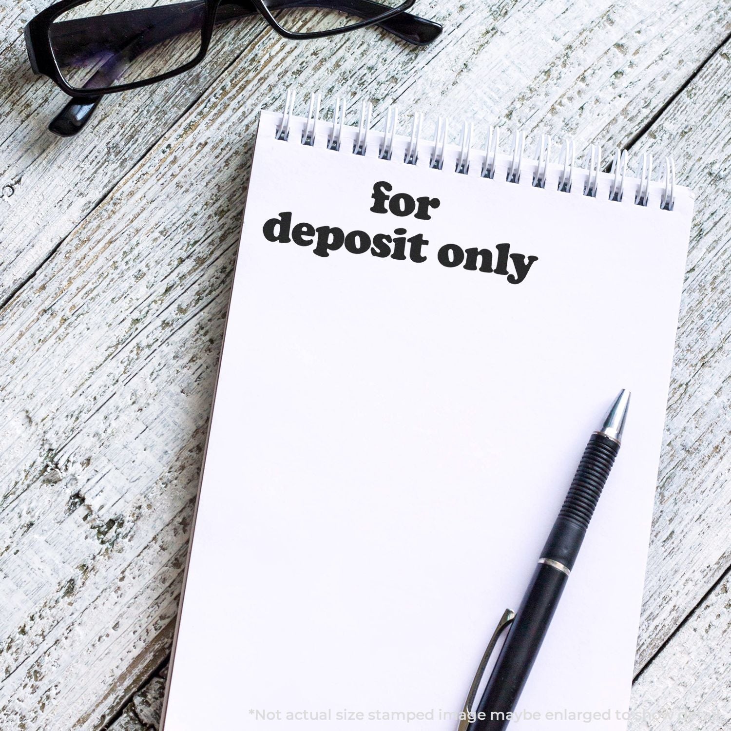 Self Inking Lowercase For Deposit Only Stamp used on a white notepad, with a pen and glasses placed nearby on a wooden surface.