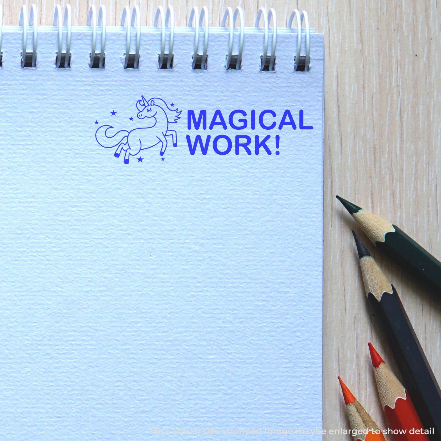 Self Inking Magical Work Stamp imprint of a unicorn and MAGICAL WORK! text on a spiral notebook, with colored pencils nearby.